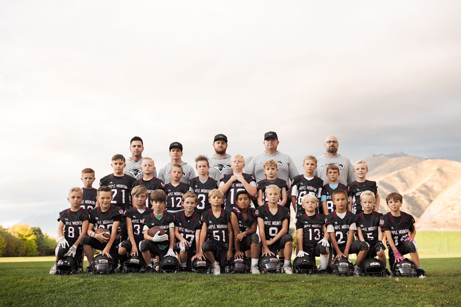 Football team members pose together on a grassy field with mountains in the background during sunset.
