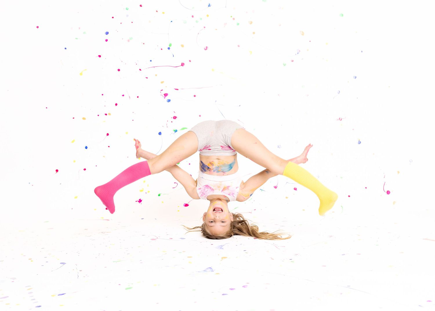 Flexible gymnast in colorful socks does backbend on white floor with confetti falling around her.