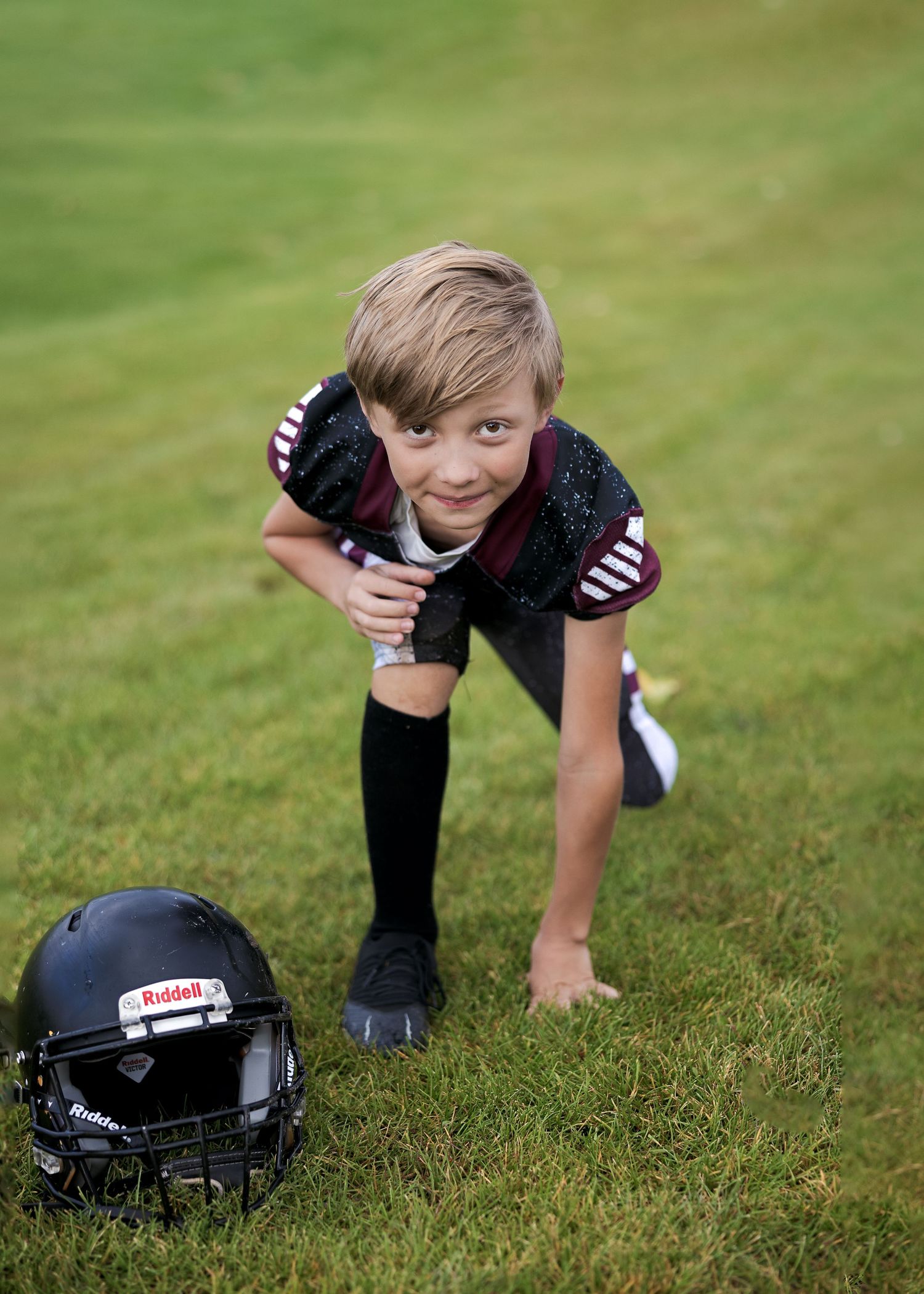 A football helmet rests on green grass while a player stretches during practice.