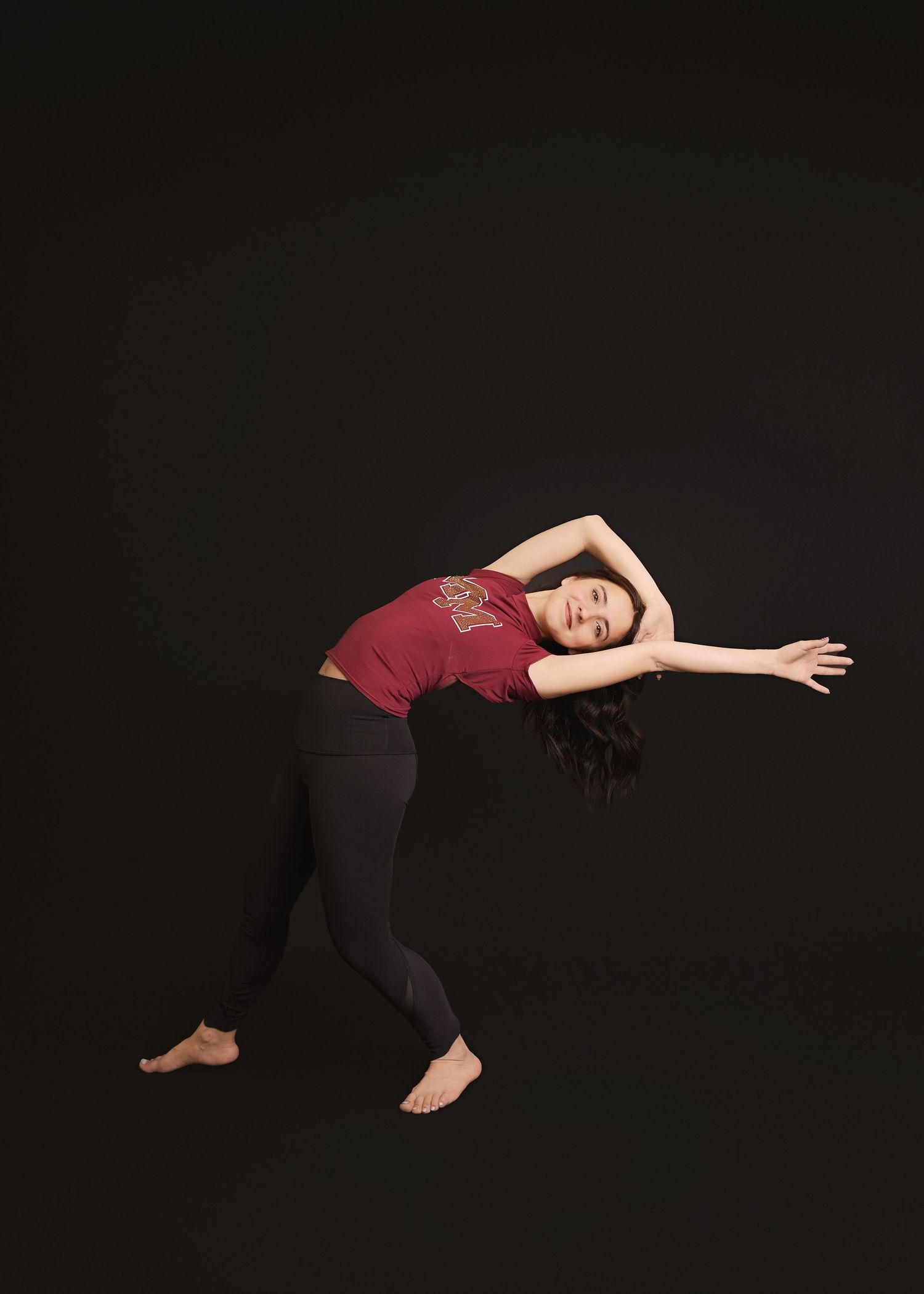 A dancer flows through a sideways stretching movement wearing a red top and black pants.