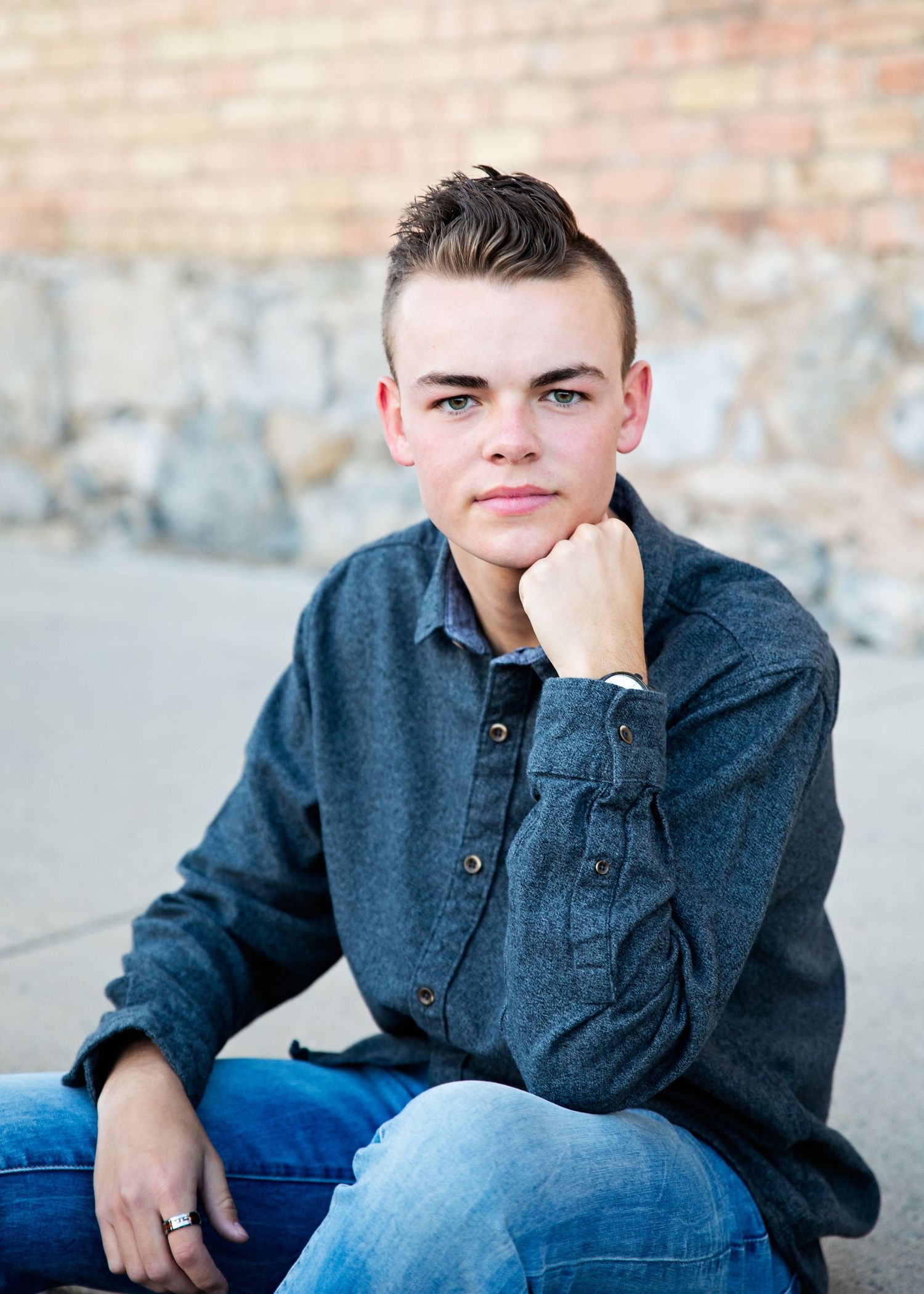 Casual portrait against brick wall wearing denim shirt and jeans with styled short hair.