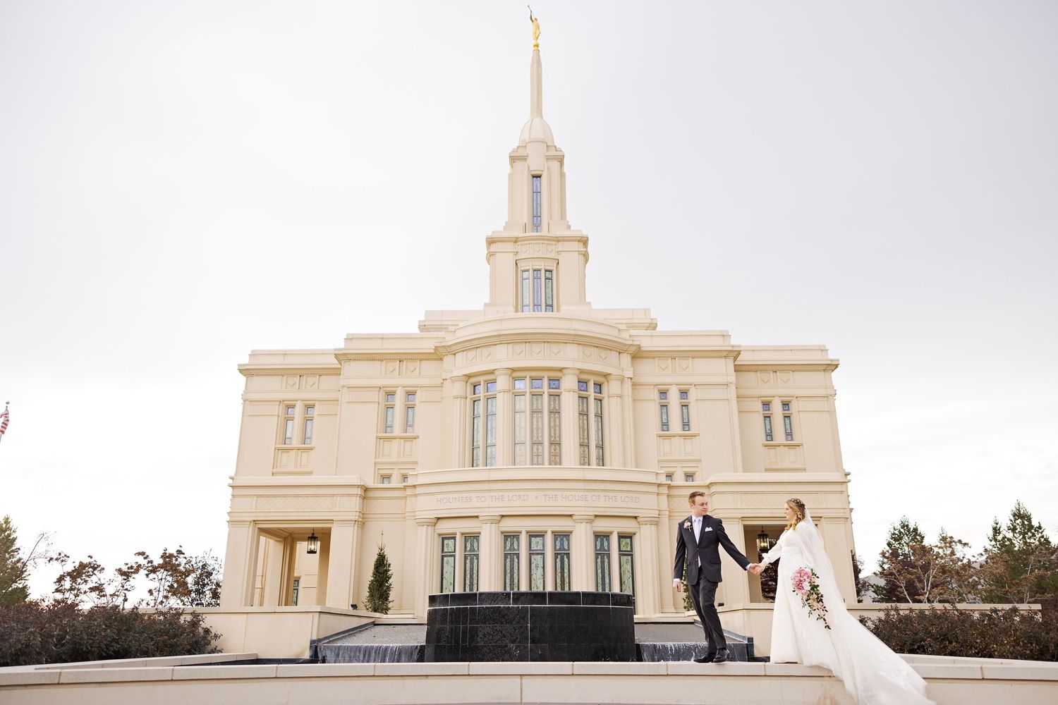 Wedding couple posing outside grand white temple building on overcast day.