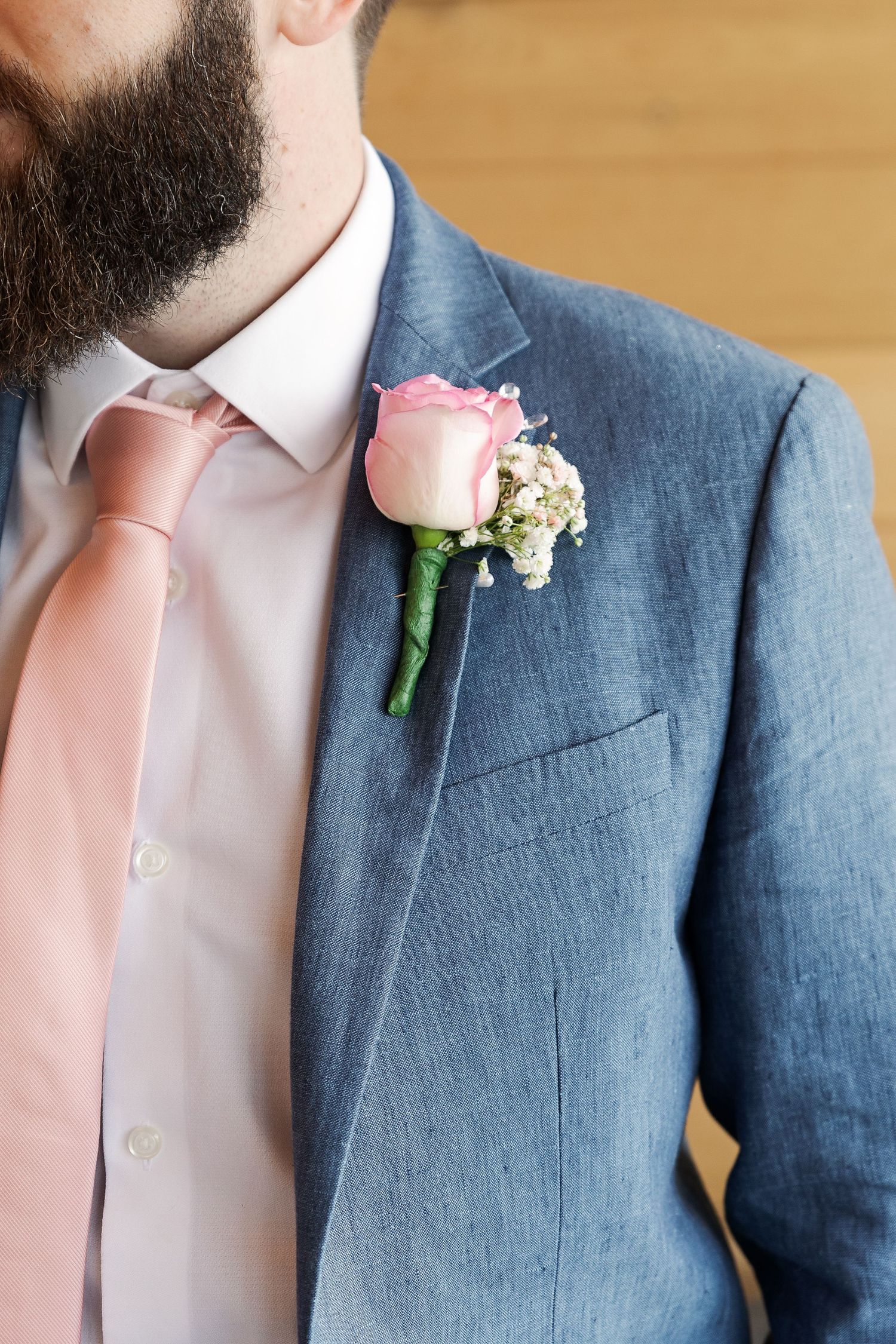 Close-up of blue suit jacket with pink rose boutonniere and blush tie.