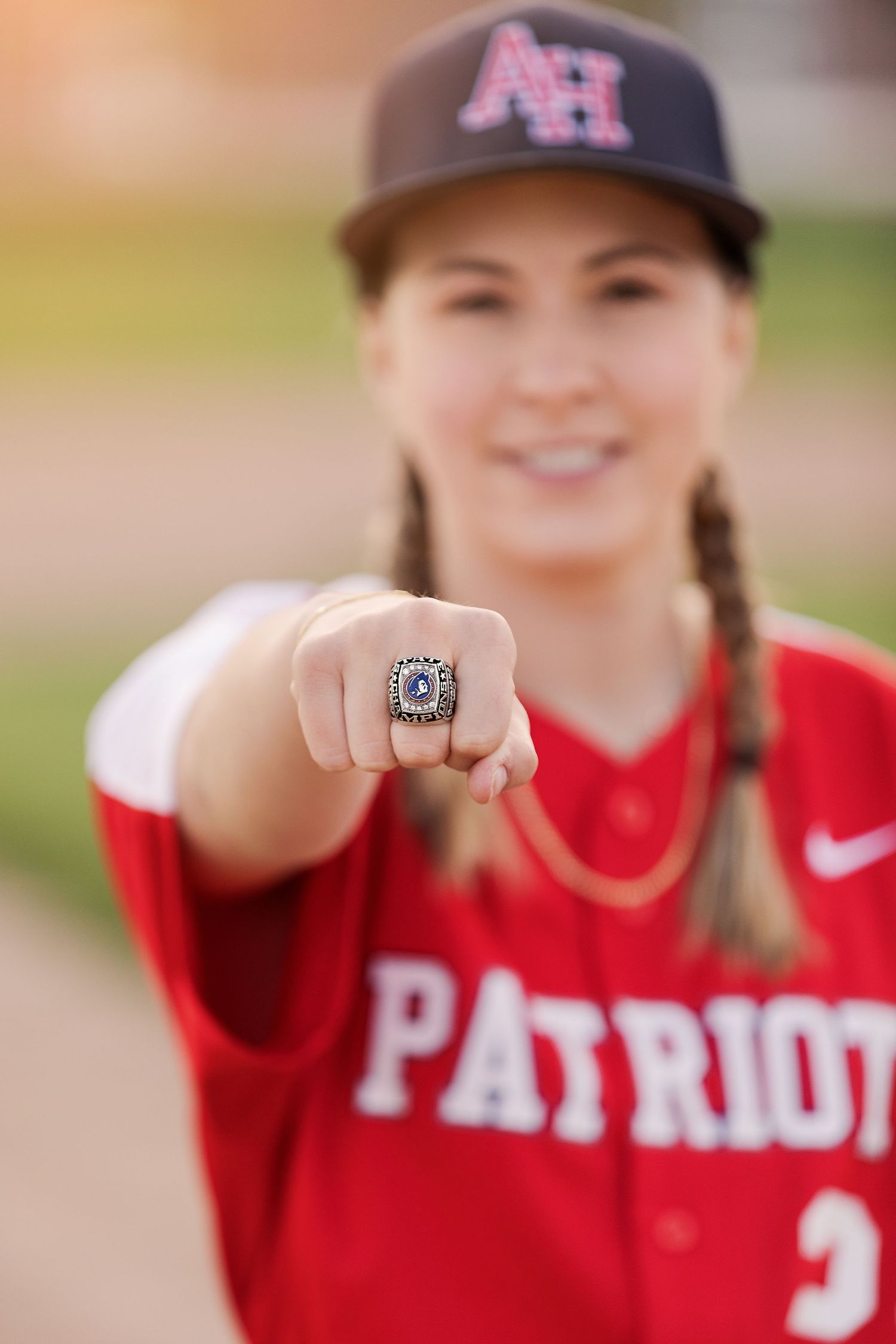 Championship ring displayed by softball player in red Patriots jersey.