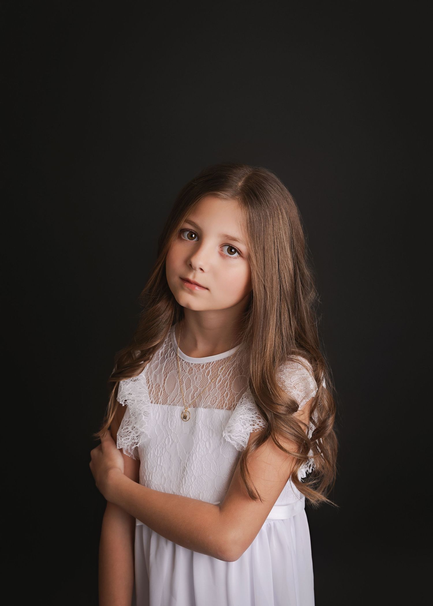 A portrait of a young person in a white lace dress against a dark background.