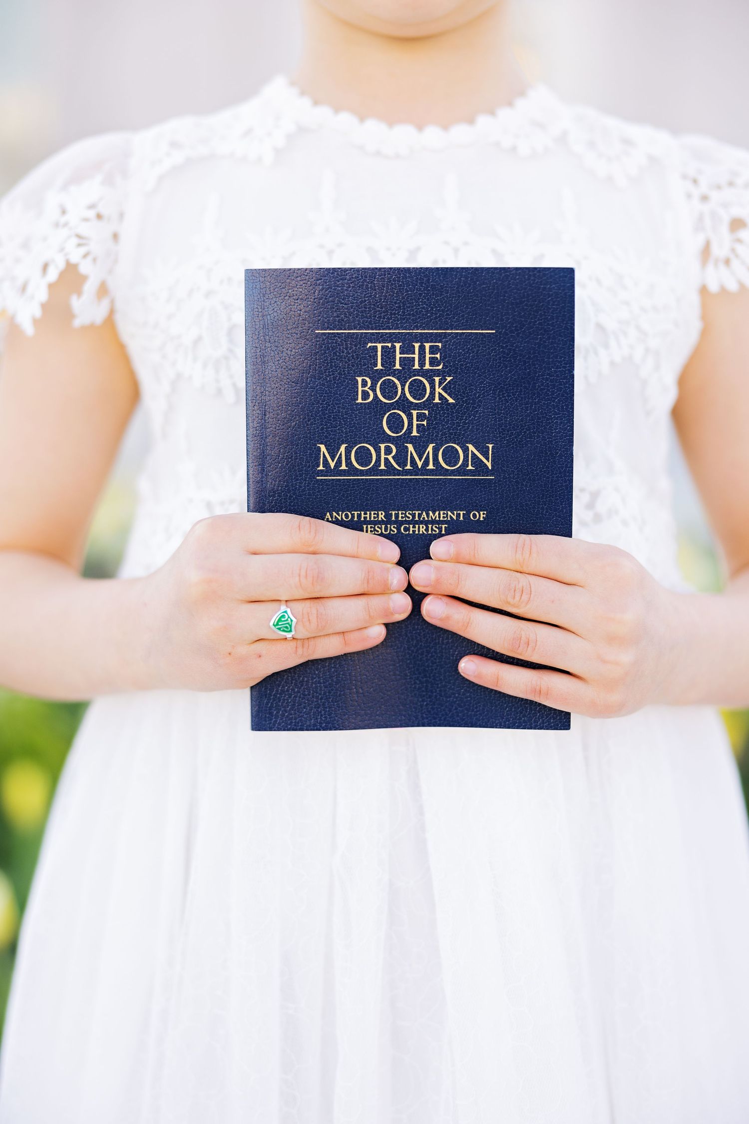 Hands holding The Book of Mormon while wearing a white lace dress.