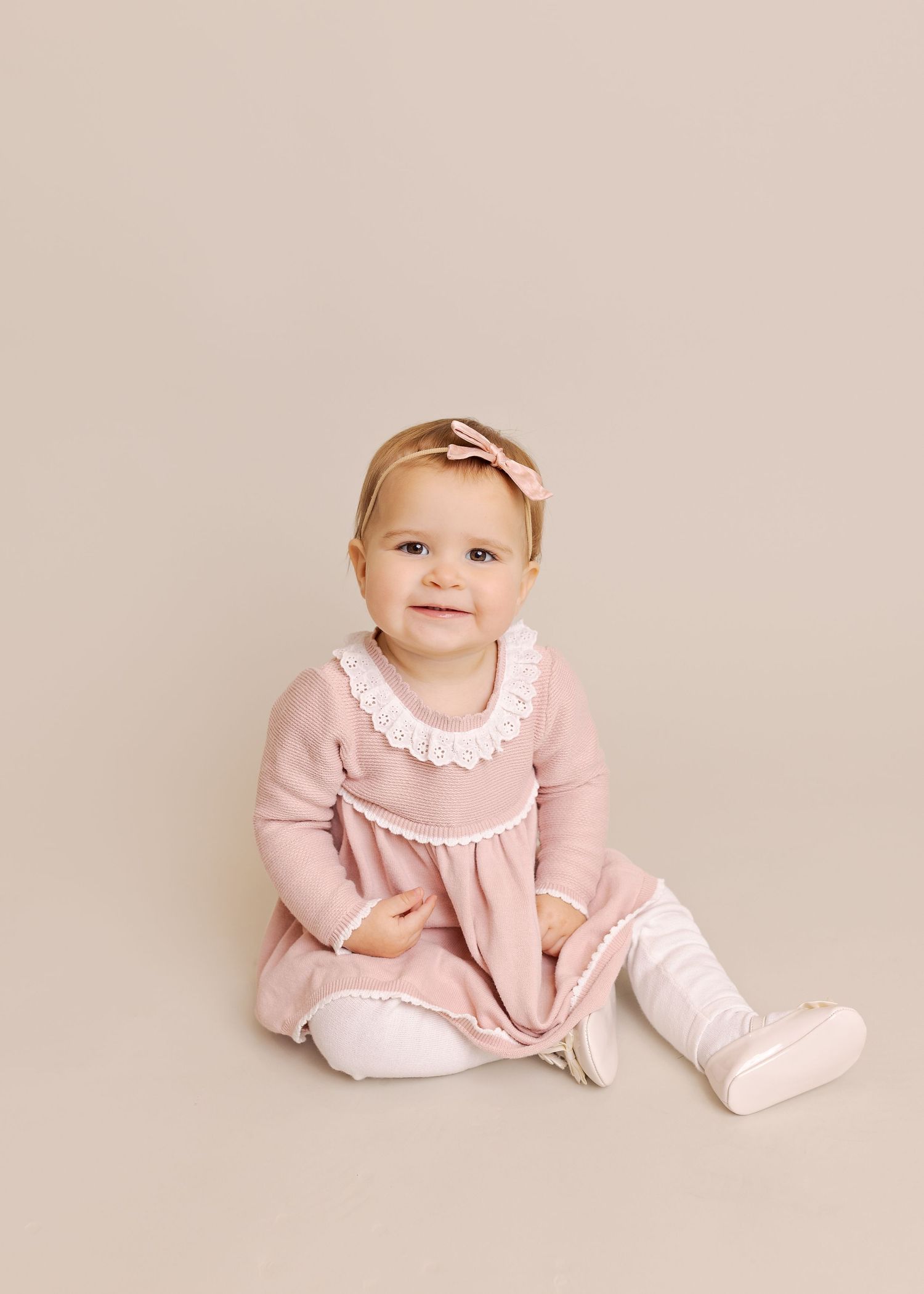 A baby wearing a pink dress and white collar sits on a light beige background in a series of four similar poses.