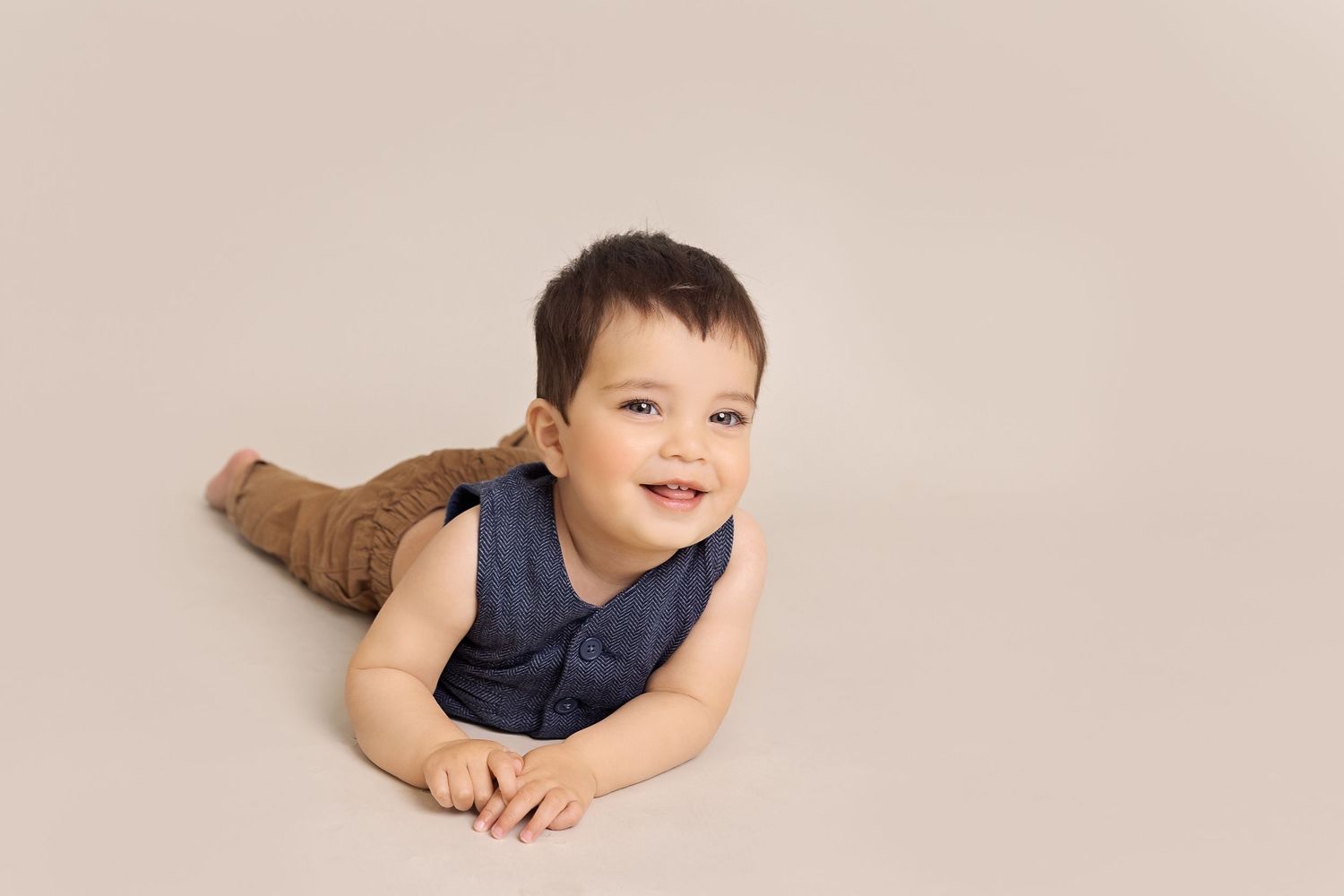Young child lying on a beige backdrop in various relaxed poses wearing navy and khaki clothing.