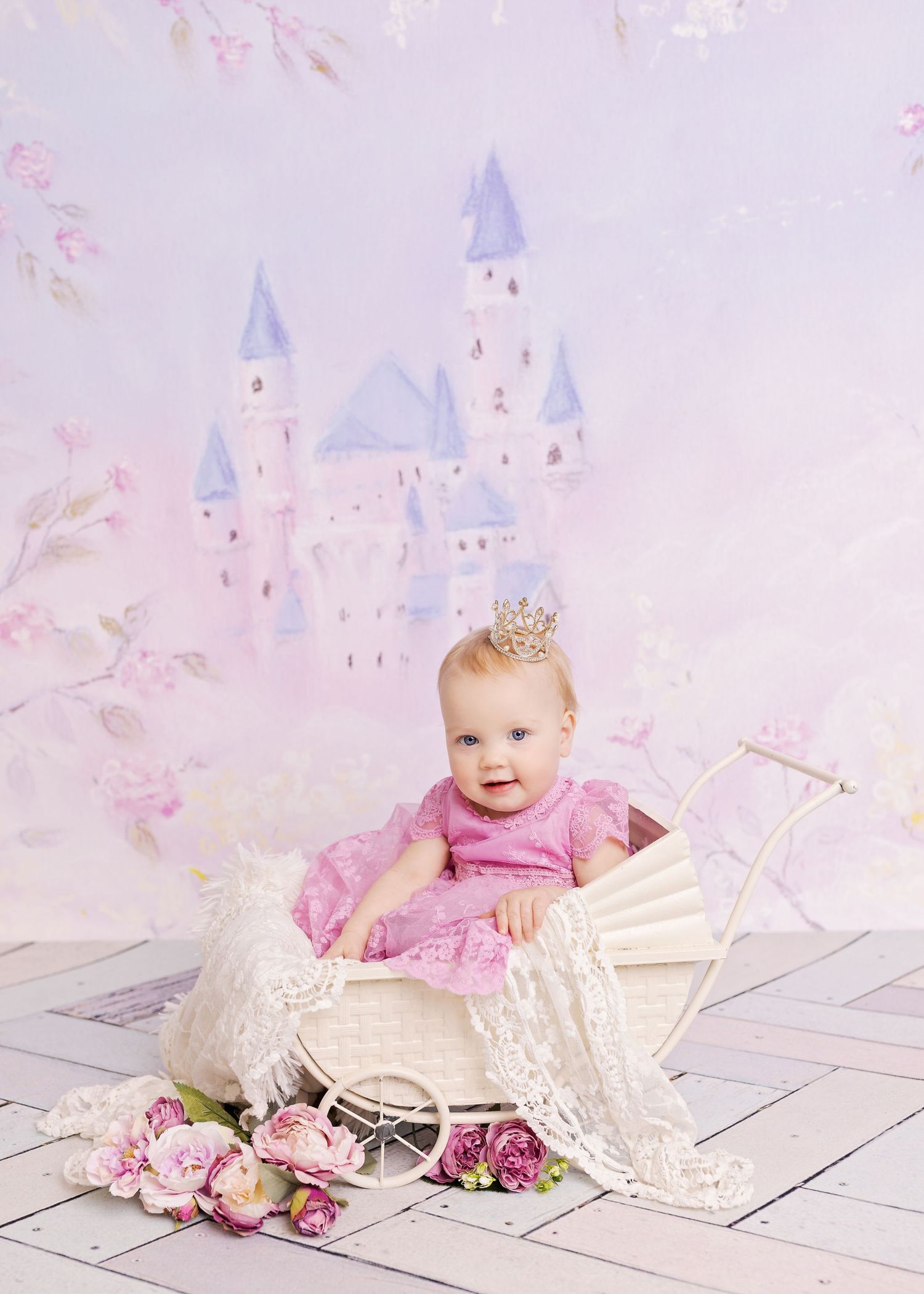 A small child in a pink dress sits in a vintage white carriage with flowers against a dreamy castle backdrop.
