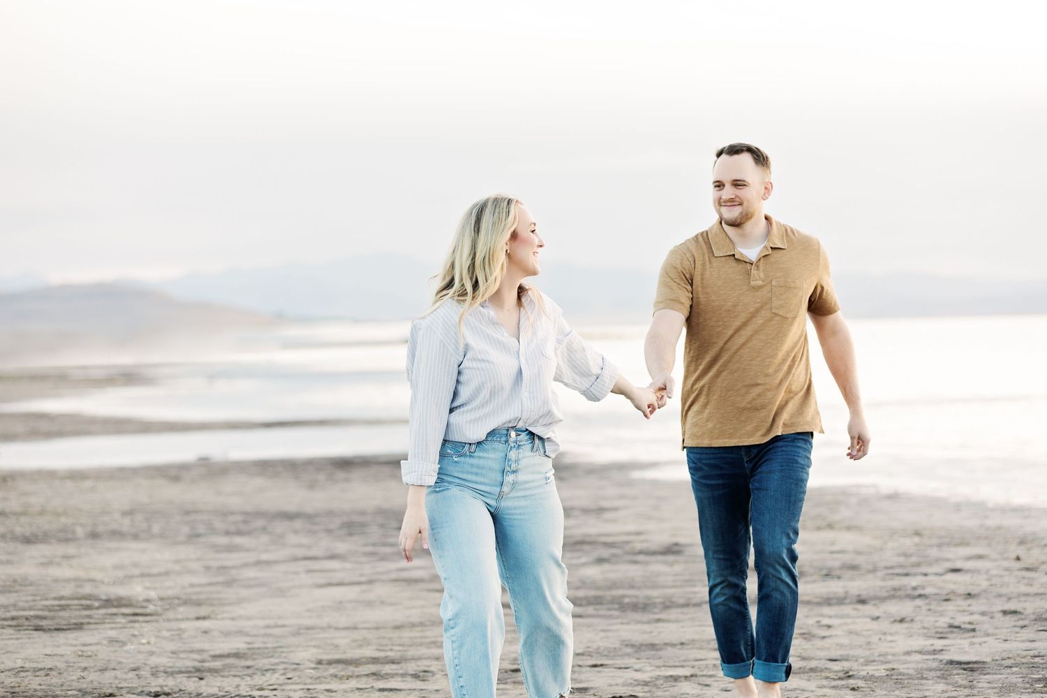 A couple walking hand in hand along a peaceful beach shore.
