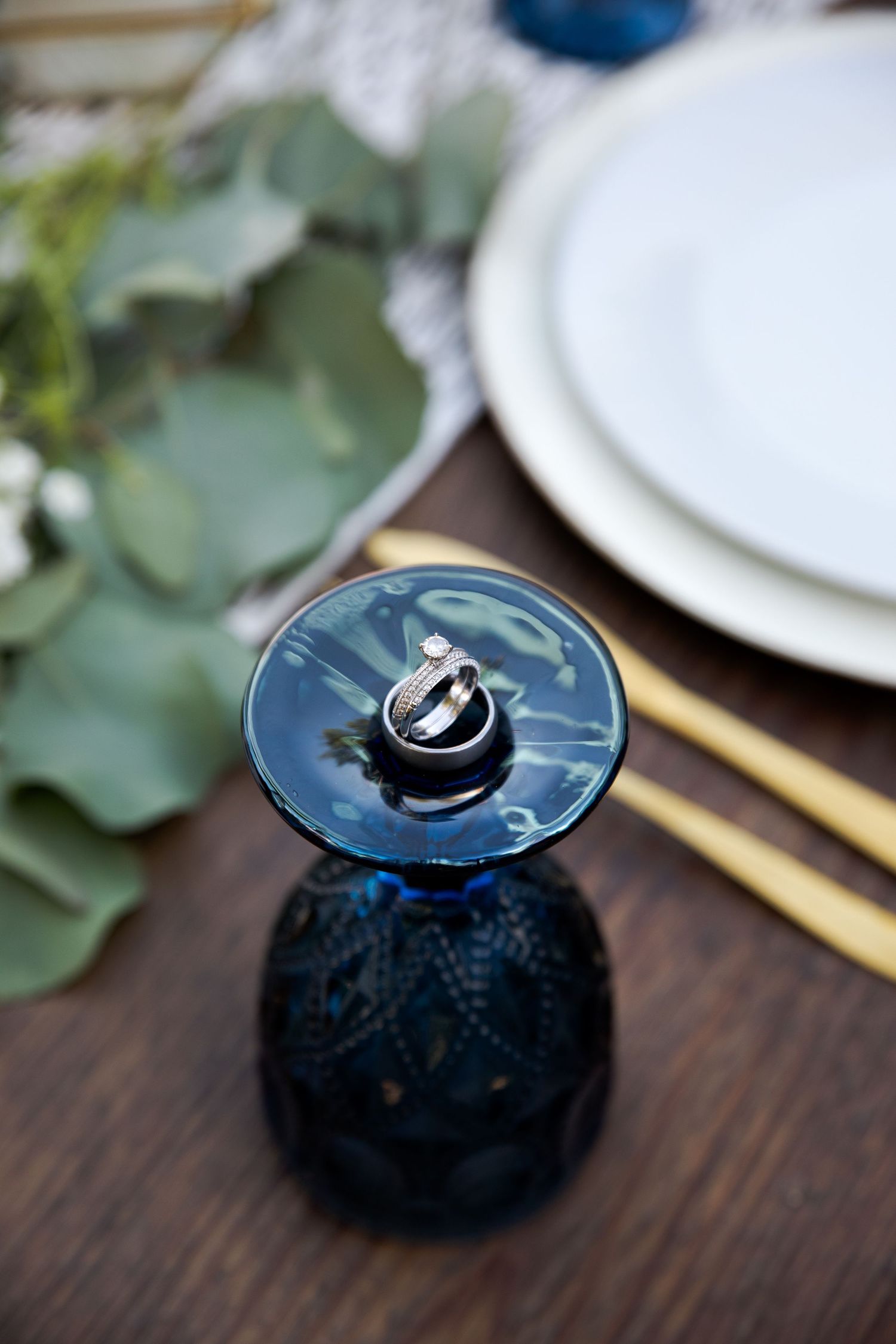 Elegant blue glass decanter on wooden table with place settings and eucalyptus.