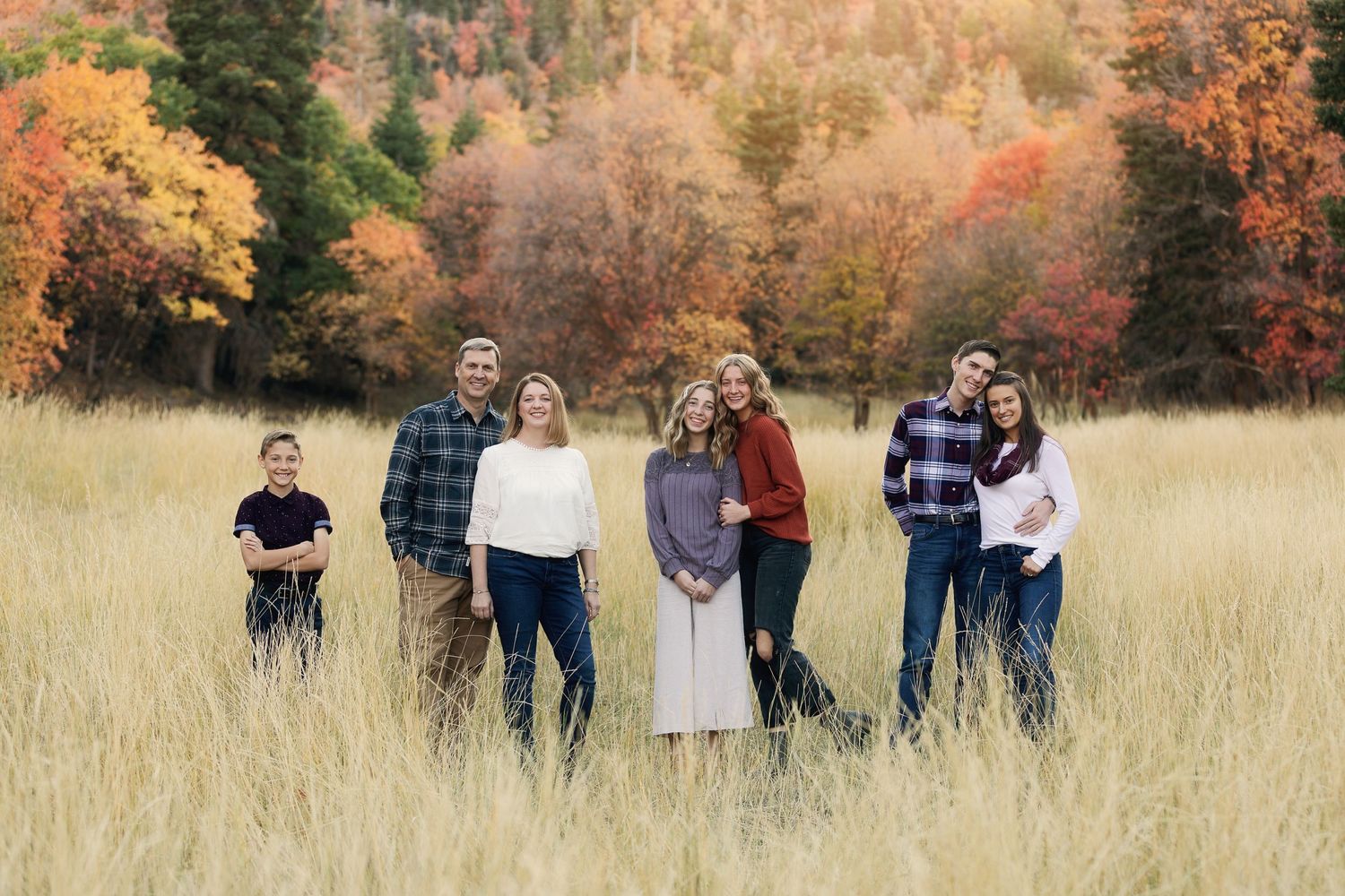 A group poses in tall golden grass with autumn foliage in the background during sunset.