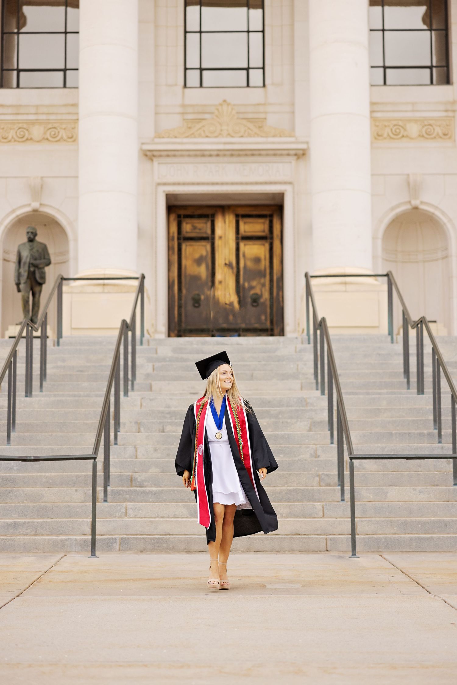 Graduate ascending stone steps of historic building in full academic regalia.