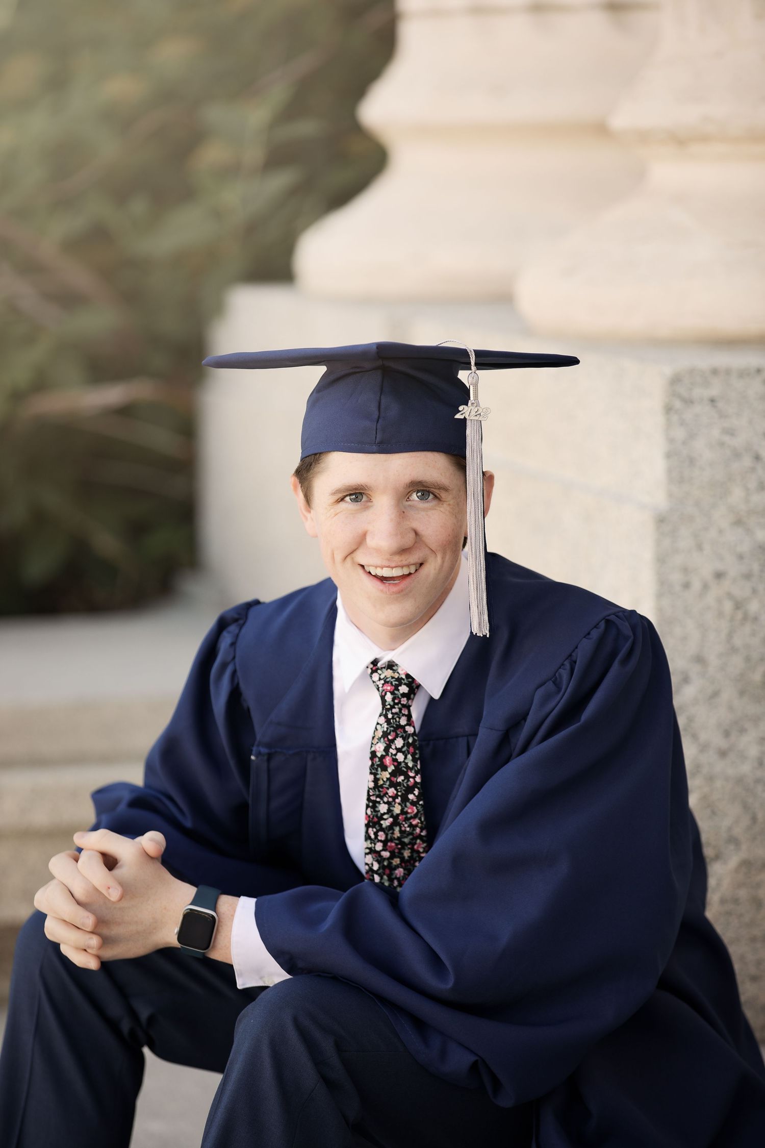 Graduate in traditional dark blue commencement regalia seated on steps.