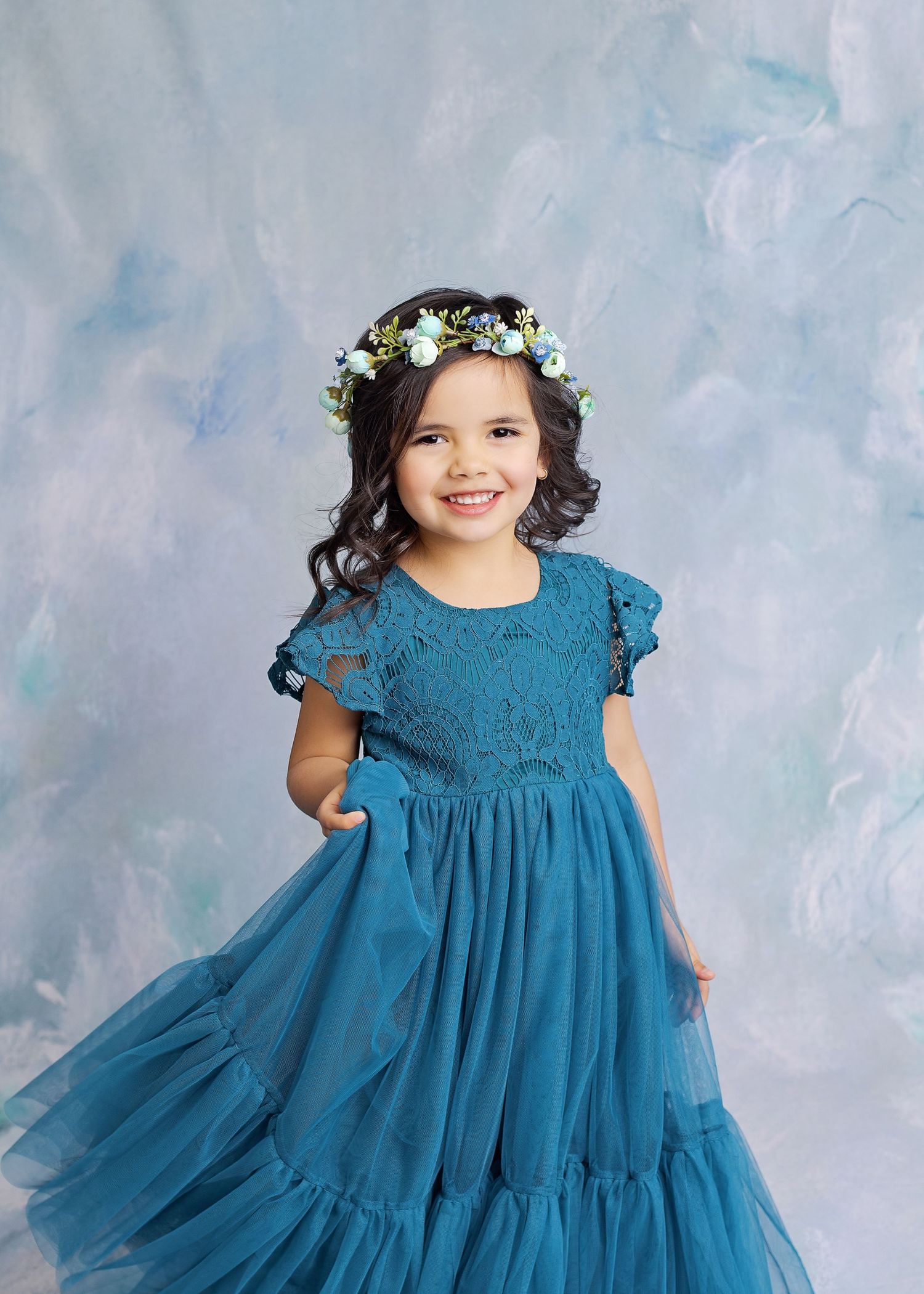 Beautiful teal lace and tulle princess dress with flutter sleeves and floral crown against a soft blue backdrop.