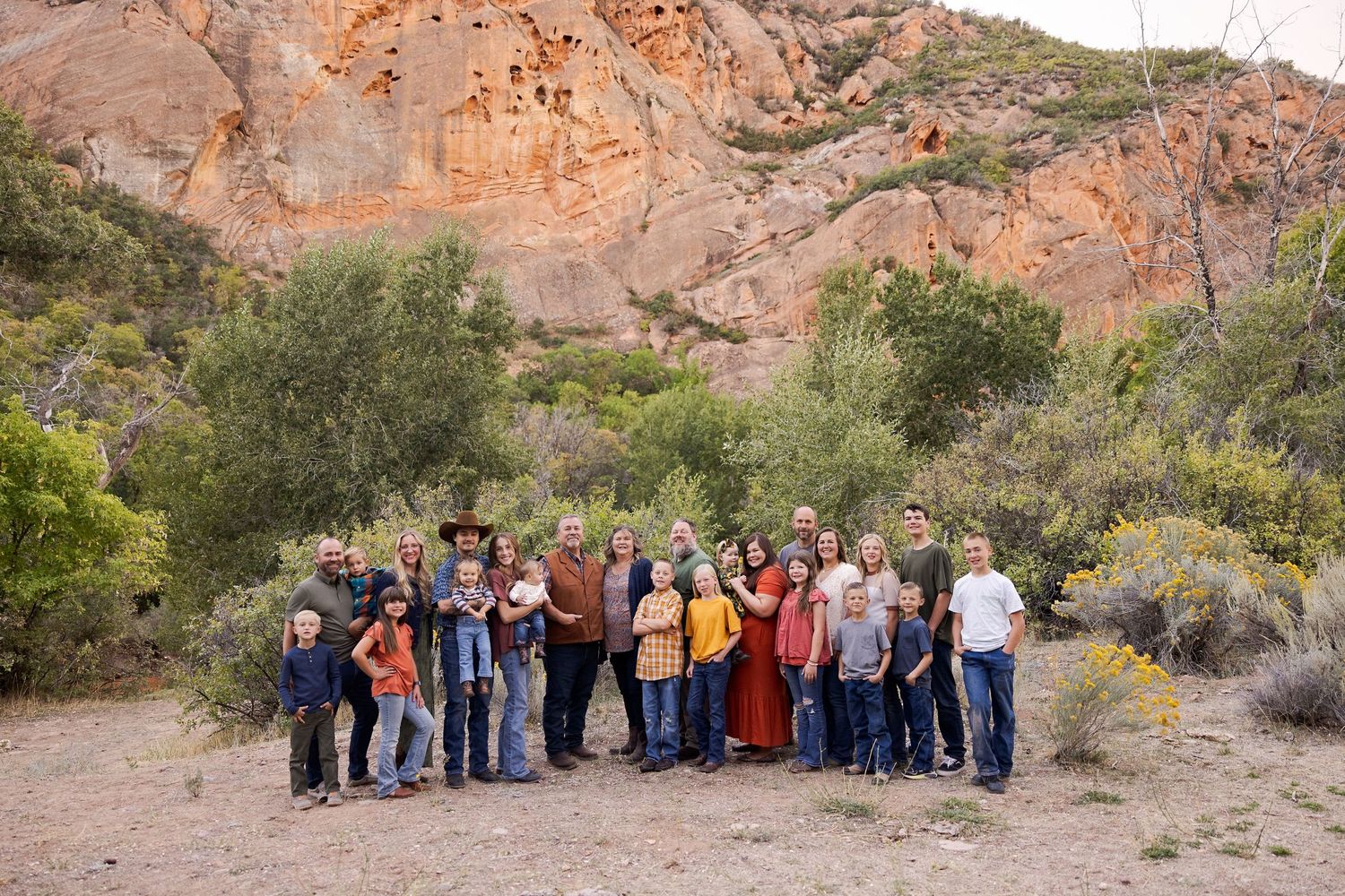 Large family group photo outdoors with red rock cliffs and desert shrubs in background.