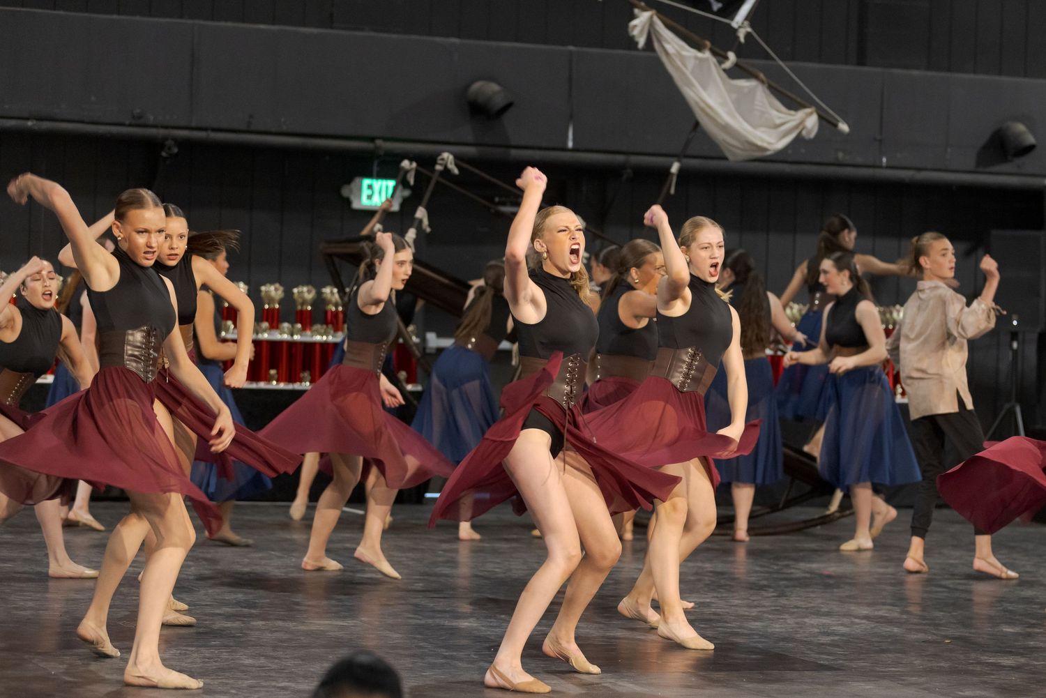 Dancers in a studio performance execute synchronized floor movements in dim lighting during a contemporary dance piece.