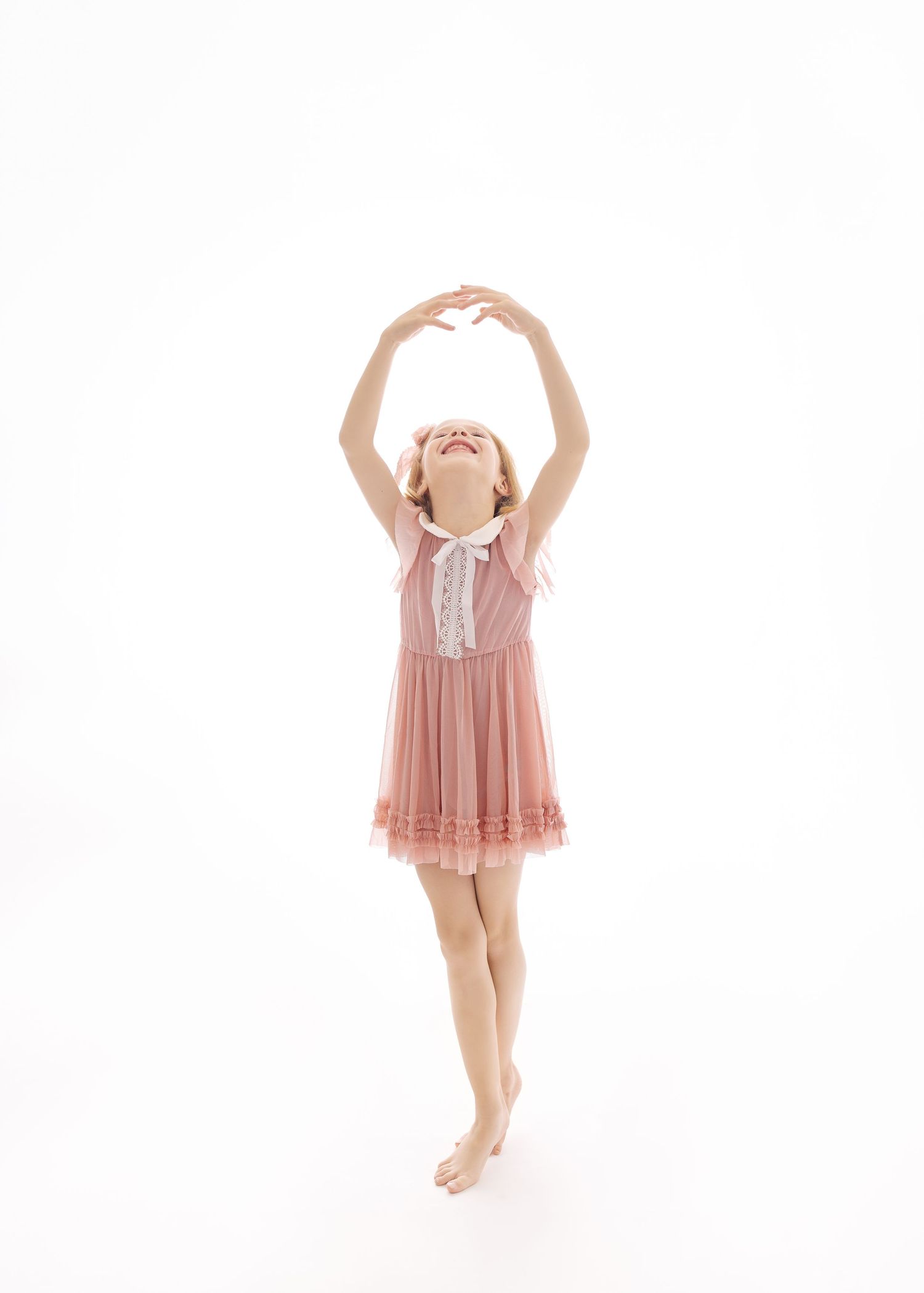 A young dancer in a pink dress jumps gracefully in a joyful sequence against a white background.
