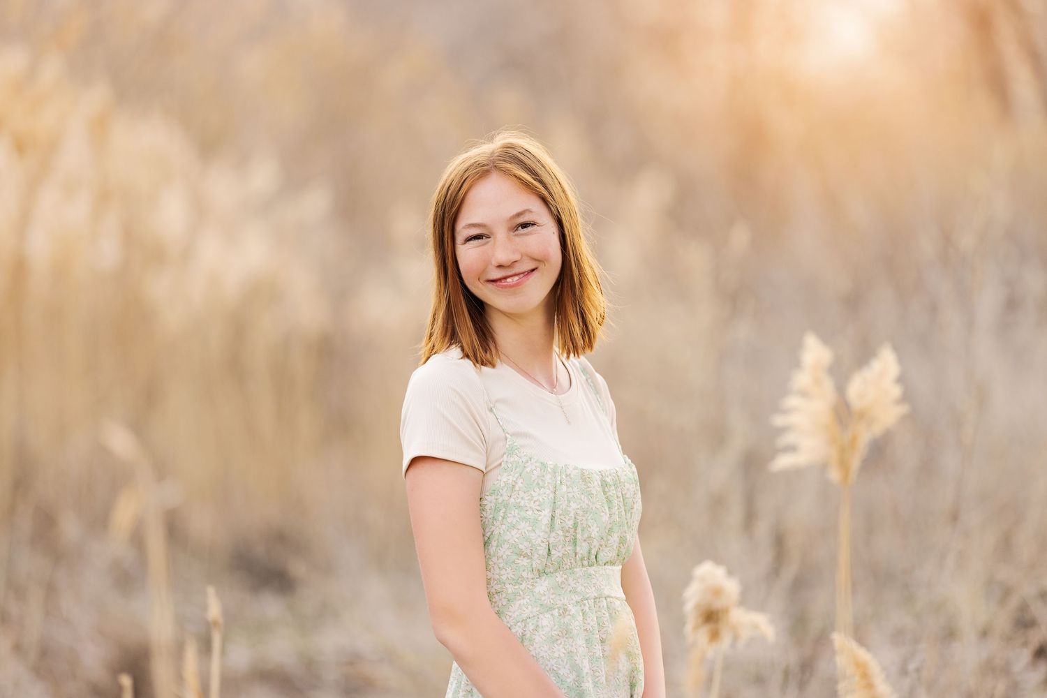 A portrait in a field of golden wheat during sunset wearing a white and mint dress.