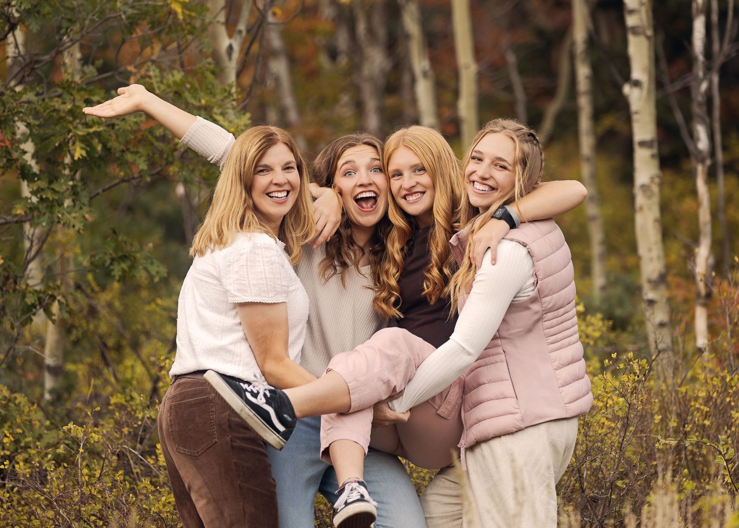 Four friends share a joyful moment together in an autumn birch forest wearing light colored clothing.