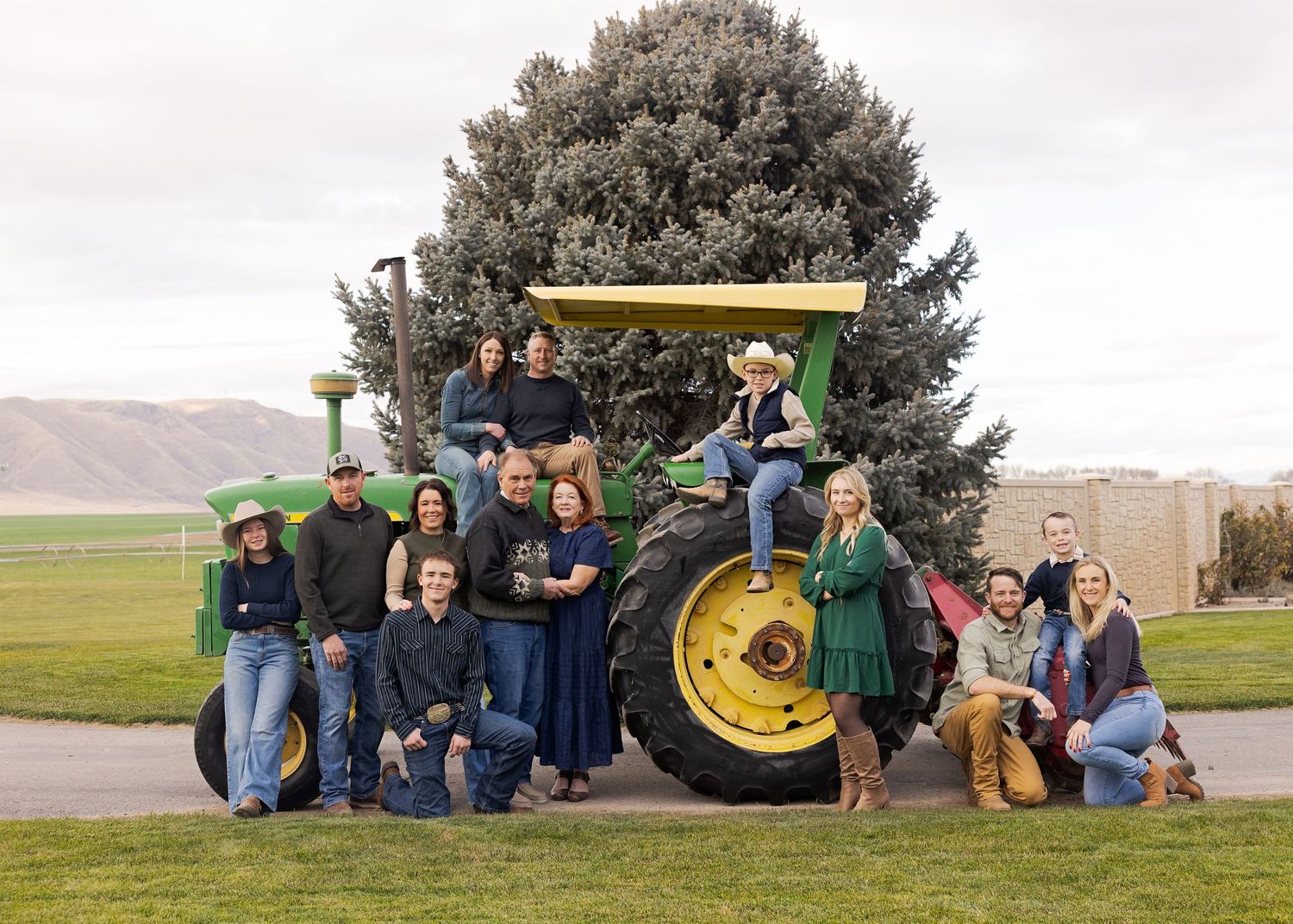 Large family group posing together around a green John Deere tractor outdoors on a farm.