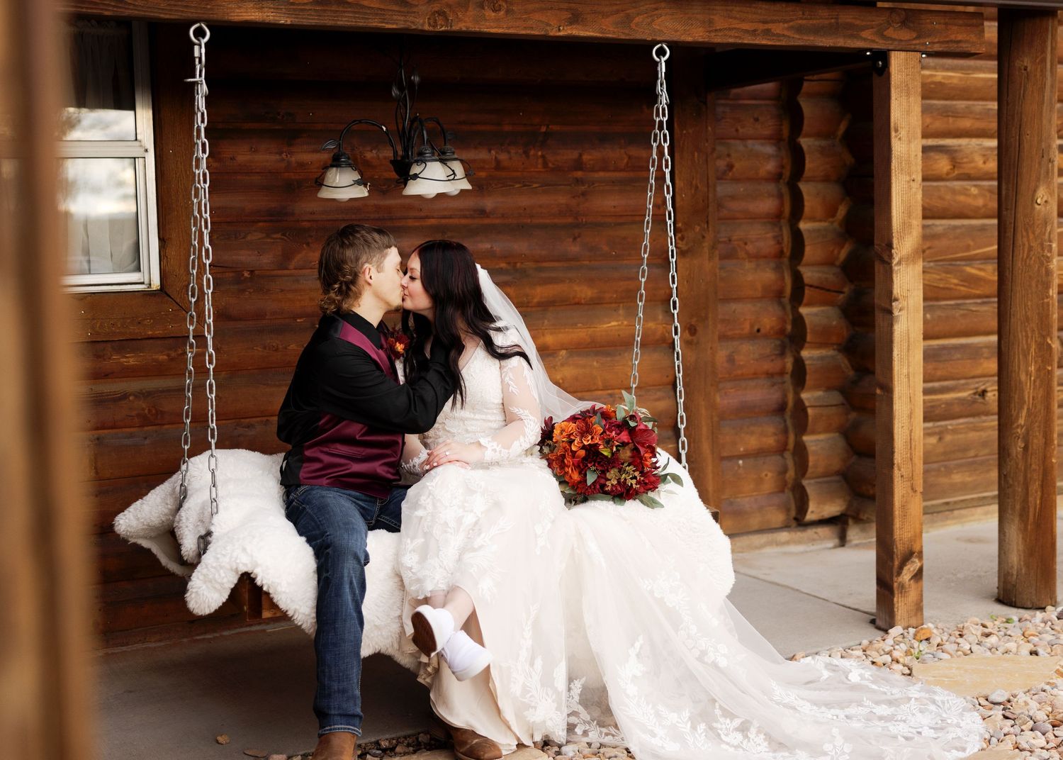 Sweet moment captured on rustic porch swing with lace wedding dress and autumn bouquet.