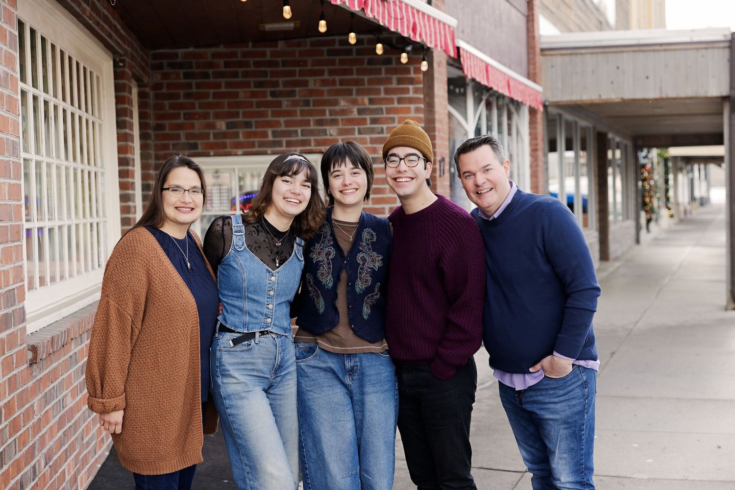 Casual group photo of friends standing together against brick wall storefront.