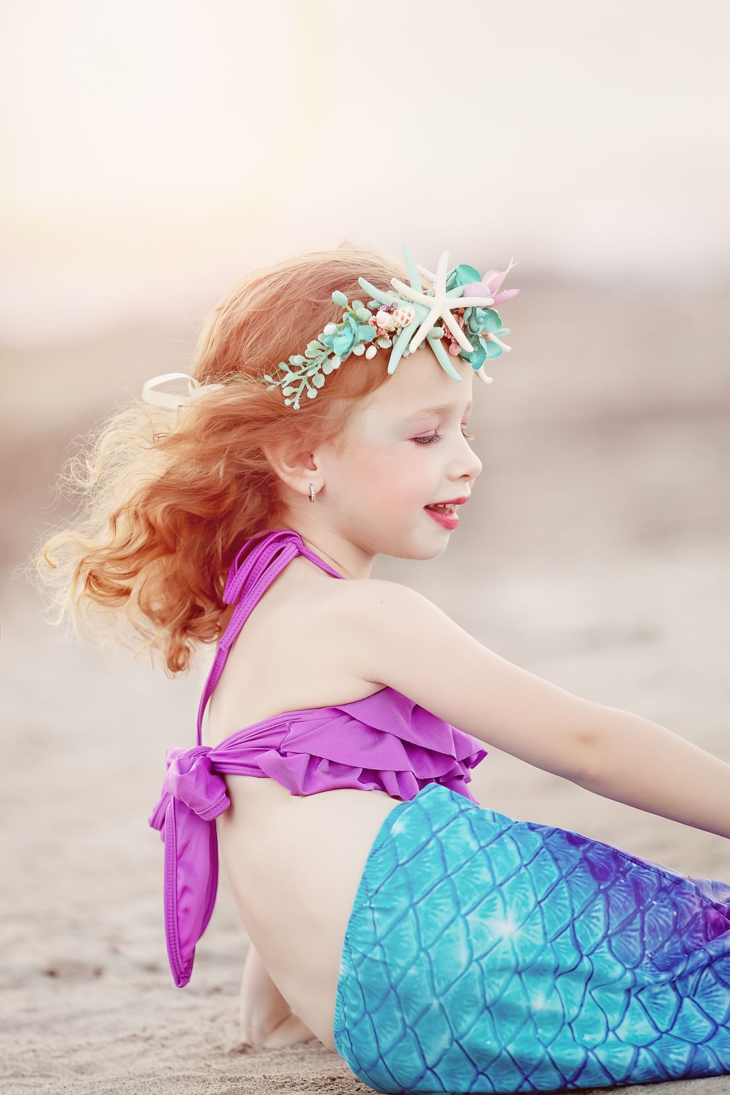 A dreamy beach photo of someone wearing a mermaid costume with flowing hair and starfish crown.