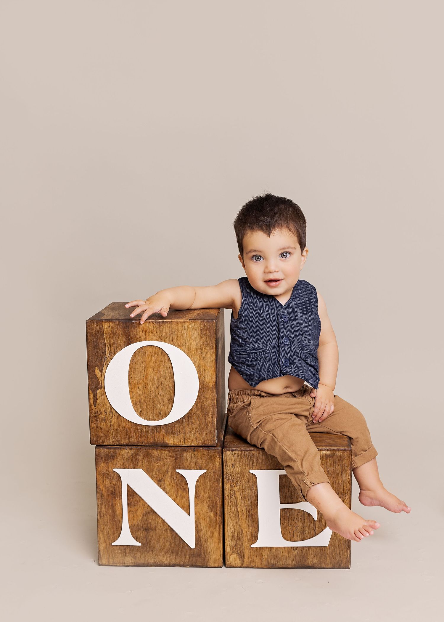 Wooden blocks with letters O-N-E arranged progressively with a child in navy shirt and brown pants sitting on them.