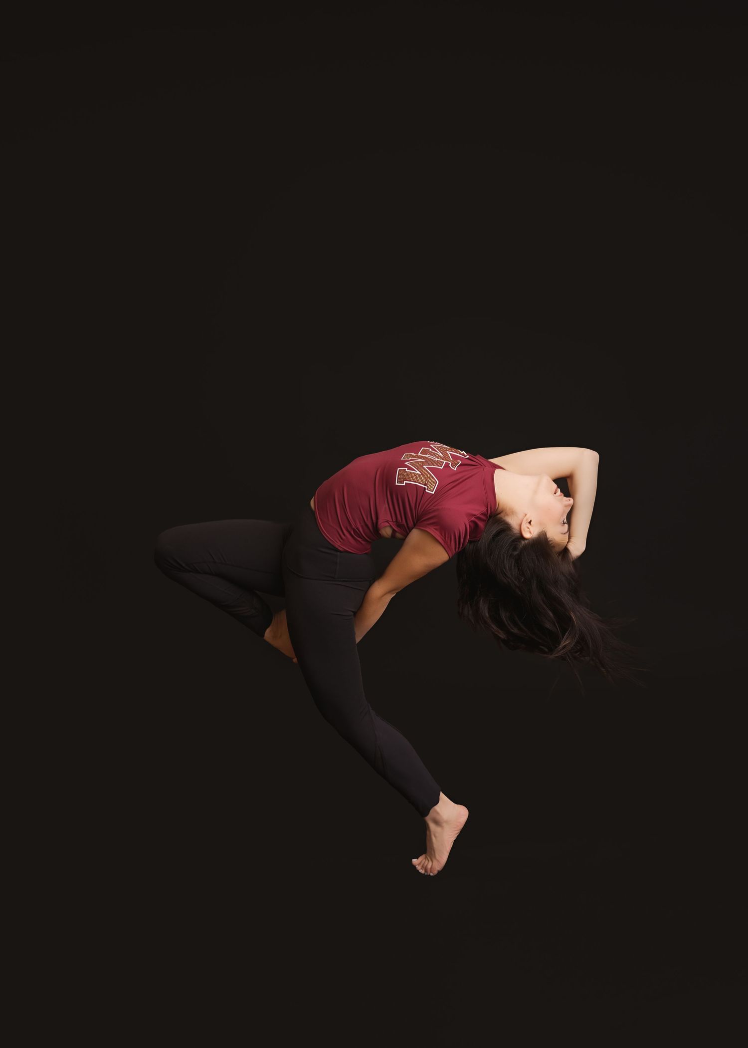 A dancer performs a graceful backbend sequence in a burgundy top against a black background.