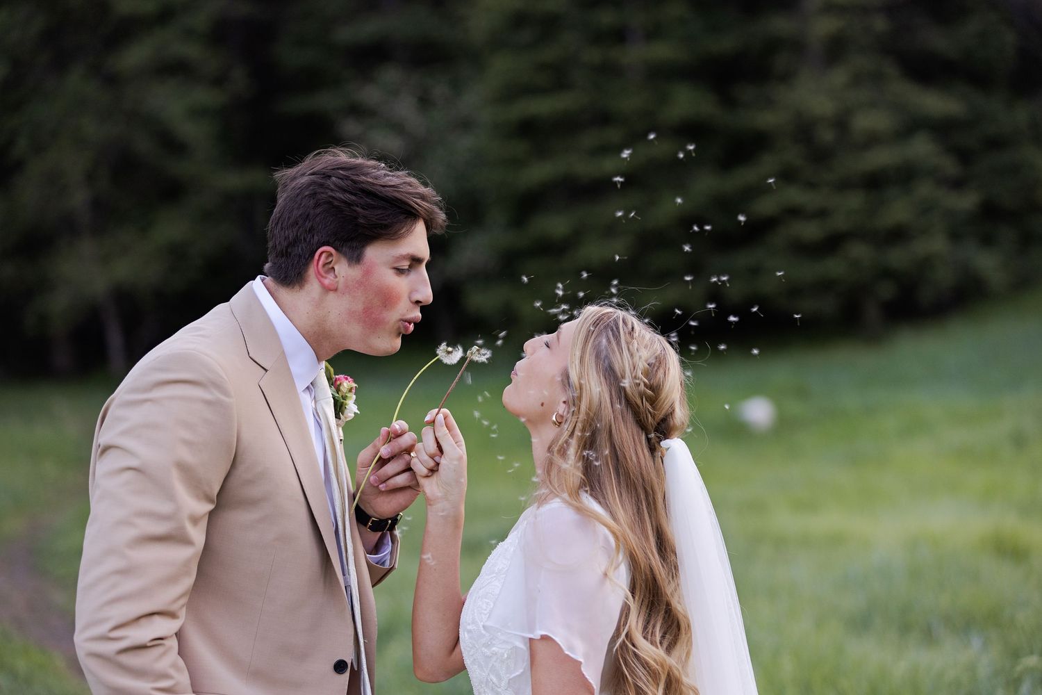 A couple shares a tender moment outdoors at a wedding with scenic greenery behind them.