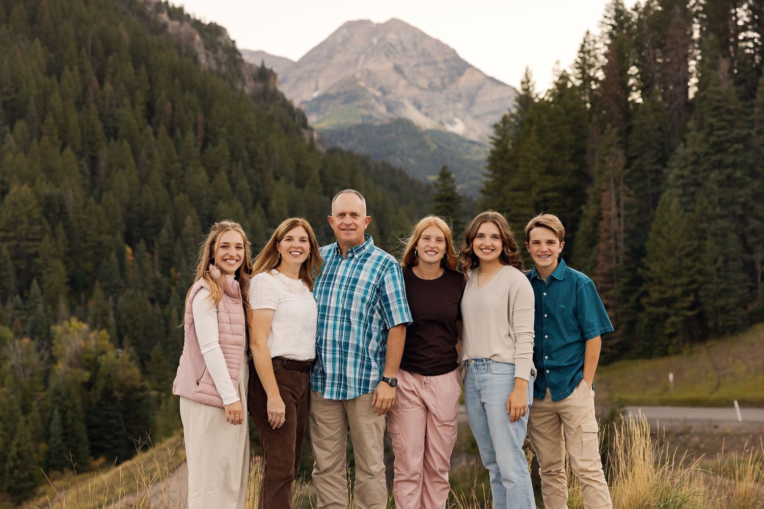 Family group photo against mountain landscape with evergreen forest backdrop.