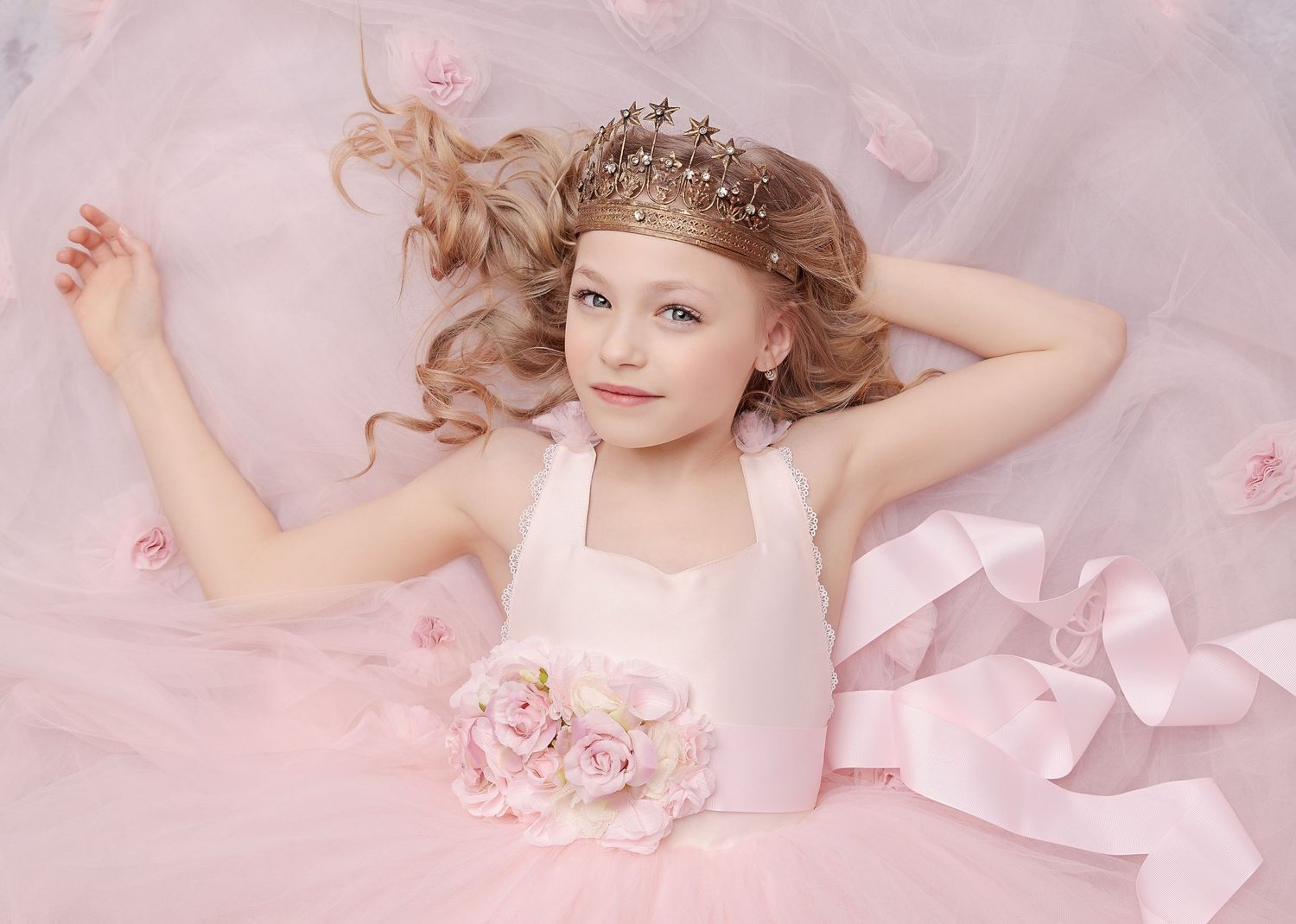 Young dancer in pink surrounded by rose petals wearing delicate crown.