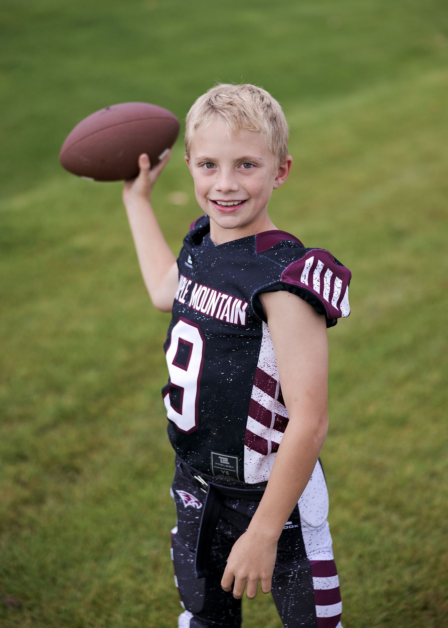 Young football player in black jersey with number 9 poses on green grass field during practice session.