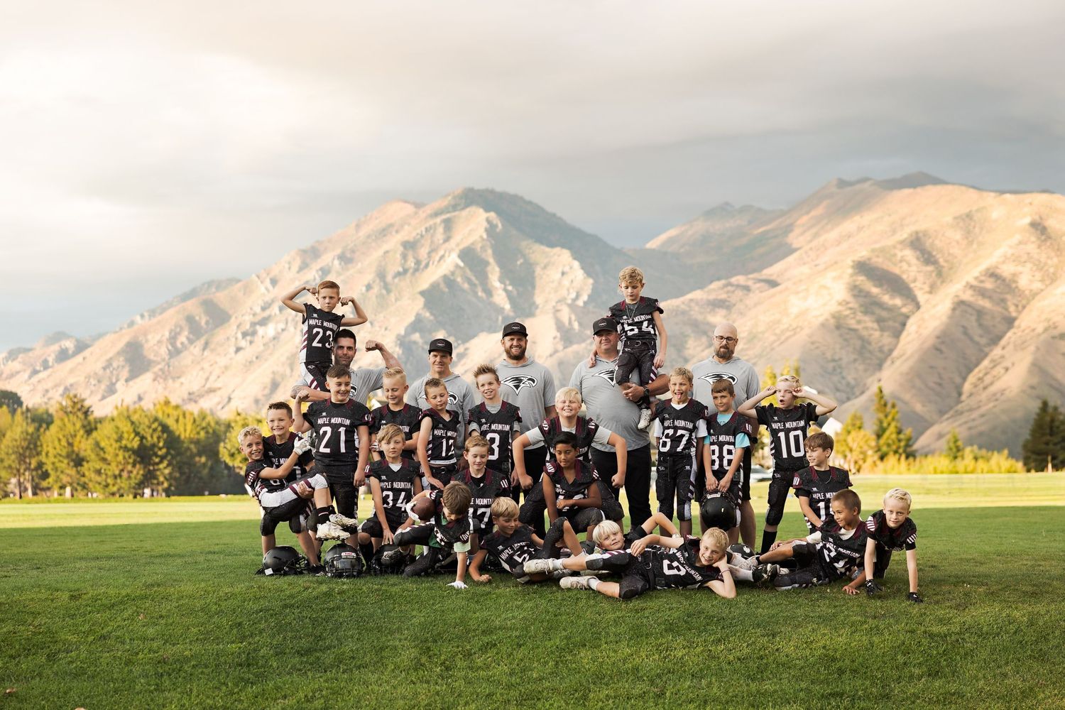 Youth football team poses together on grass field with scenic mountain backdrop during golden hour.