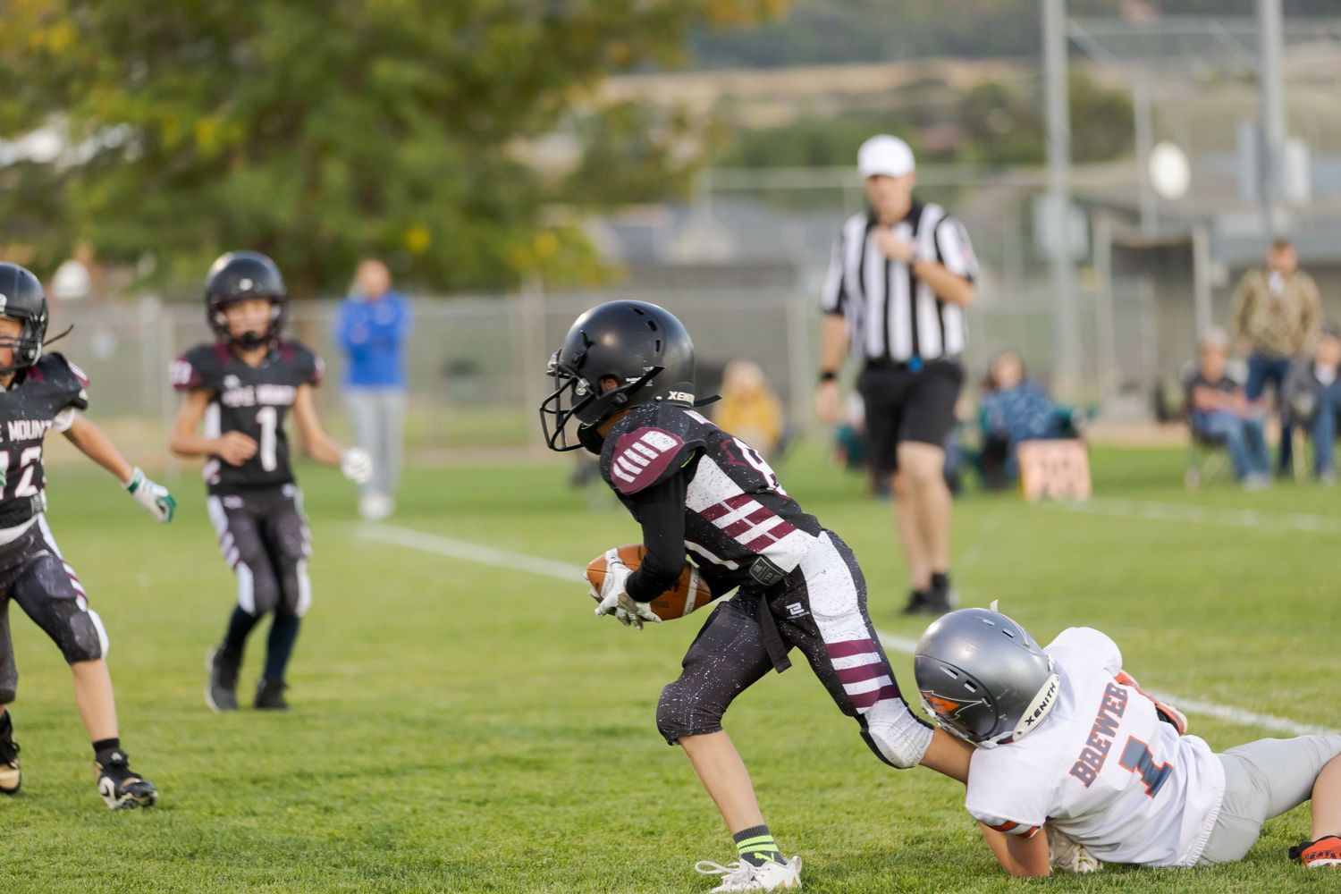 A football player in black uniform tackles an opposing player in white during a game on a grass field.
