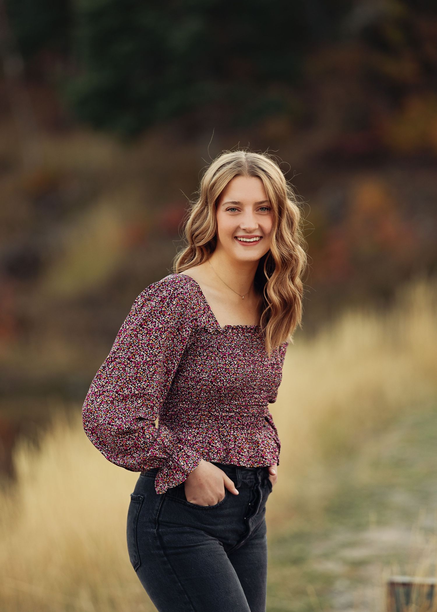 Casual portrait in floral print top with long wavy hair against autumn background.