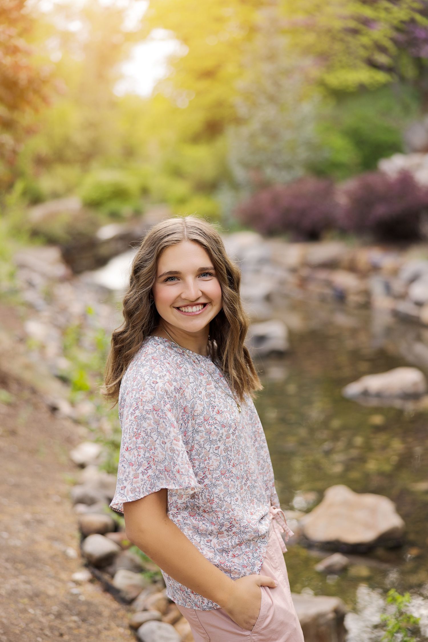 Portrait by rocky stream with sunlit foliage in background.