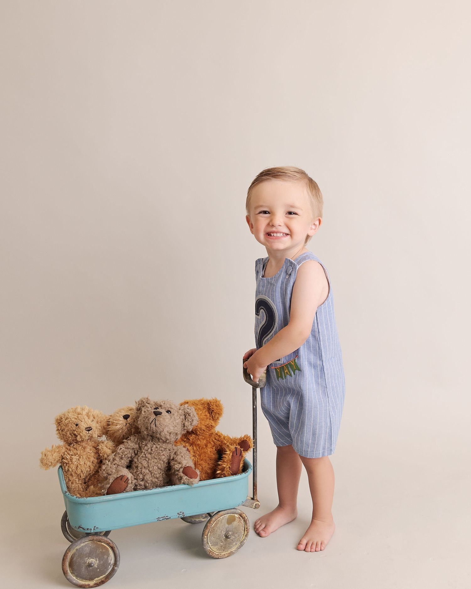 A small child in blue overalls pulling a vintage turquoise wagon filled with teddy bears.