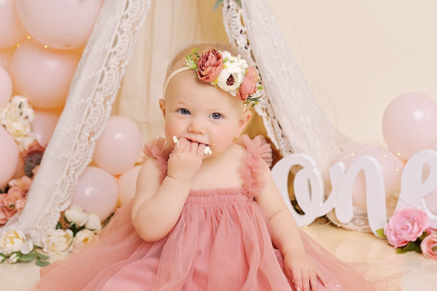 A lovely first birthday celebration setup with pink tulle dress, floral crown, and soft pastel balloon decorations.
