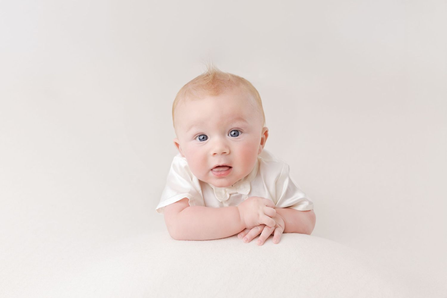 Baby in white outfit on light background with curious expression.