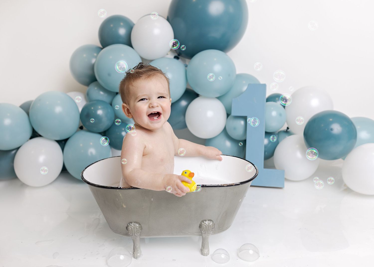 Baby bathtub photo session with blue and white balloon decorations creating a dreamy atmosphere.