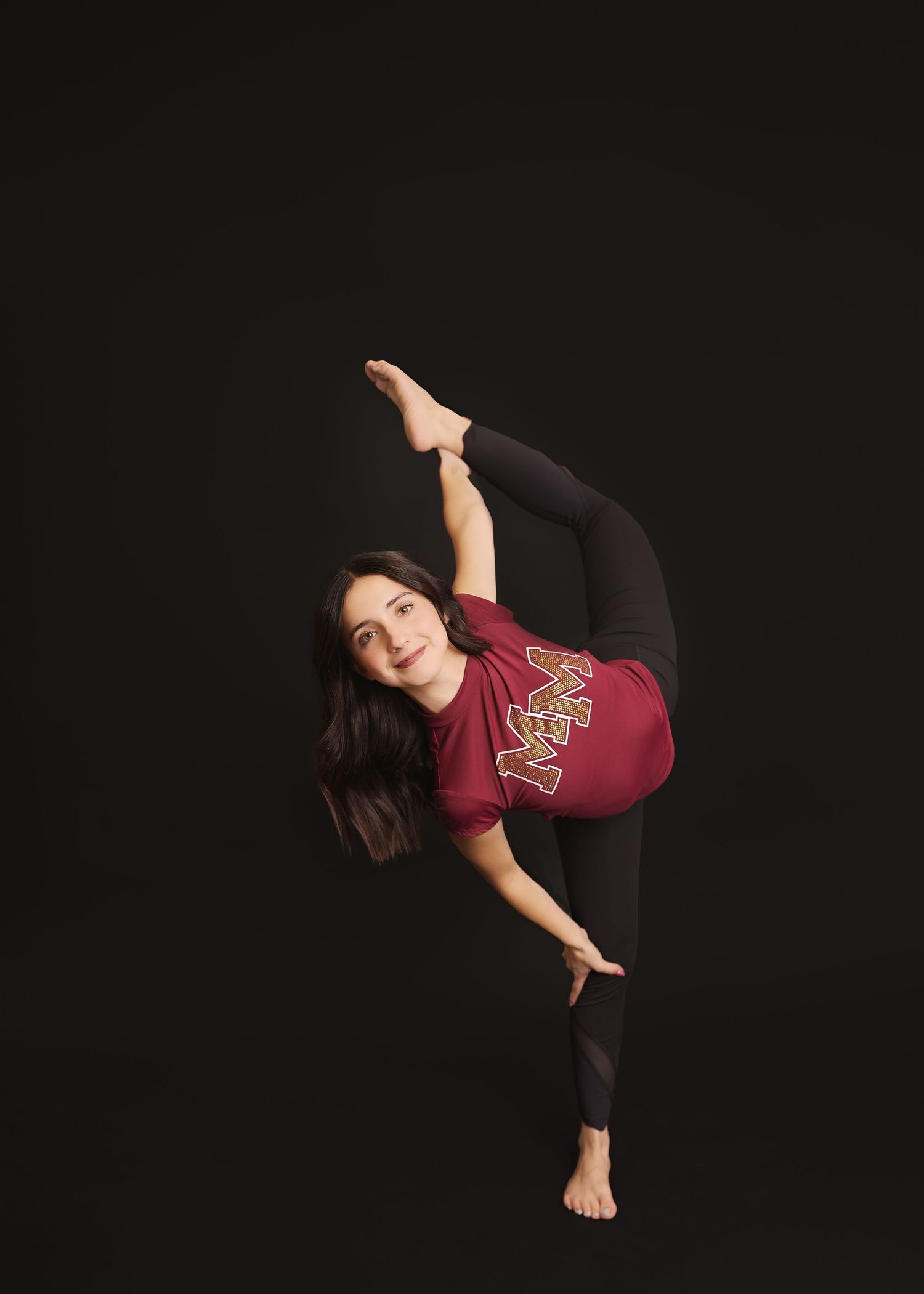 Dancer in red top performs a standing split pose against a black background while reaching toward the floor.