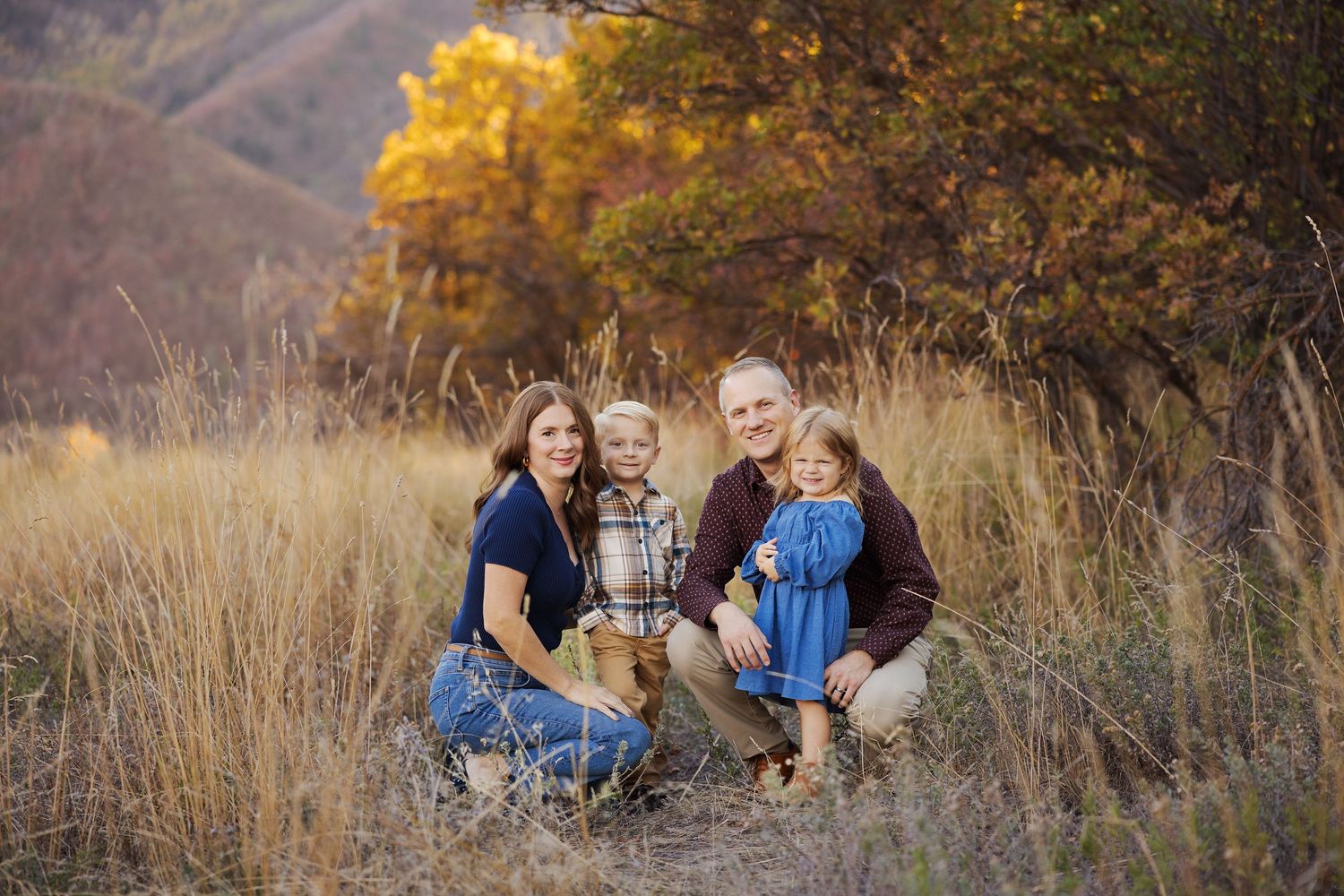 Family portrait taken in tall autumn grass with mountains in the background.