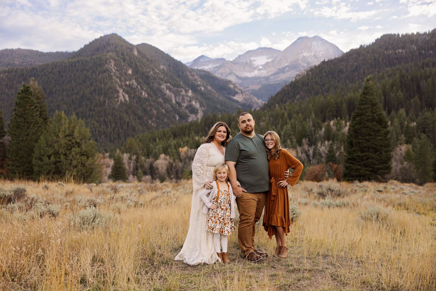 Three people stand together against a backdrop of majestic mountain peaks and autumn fields.