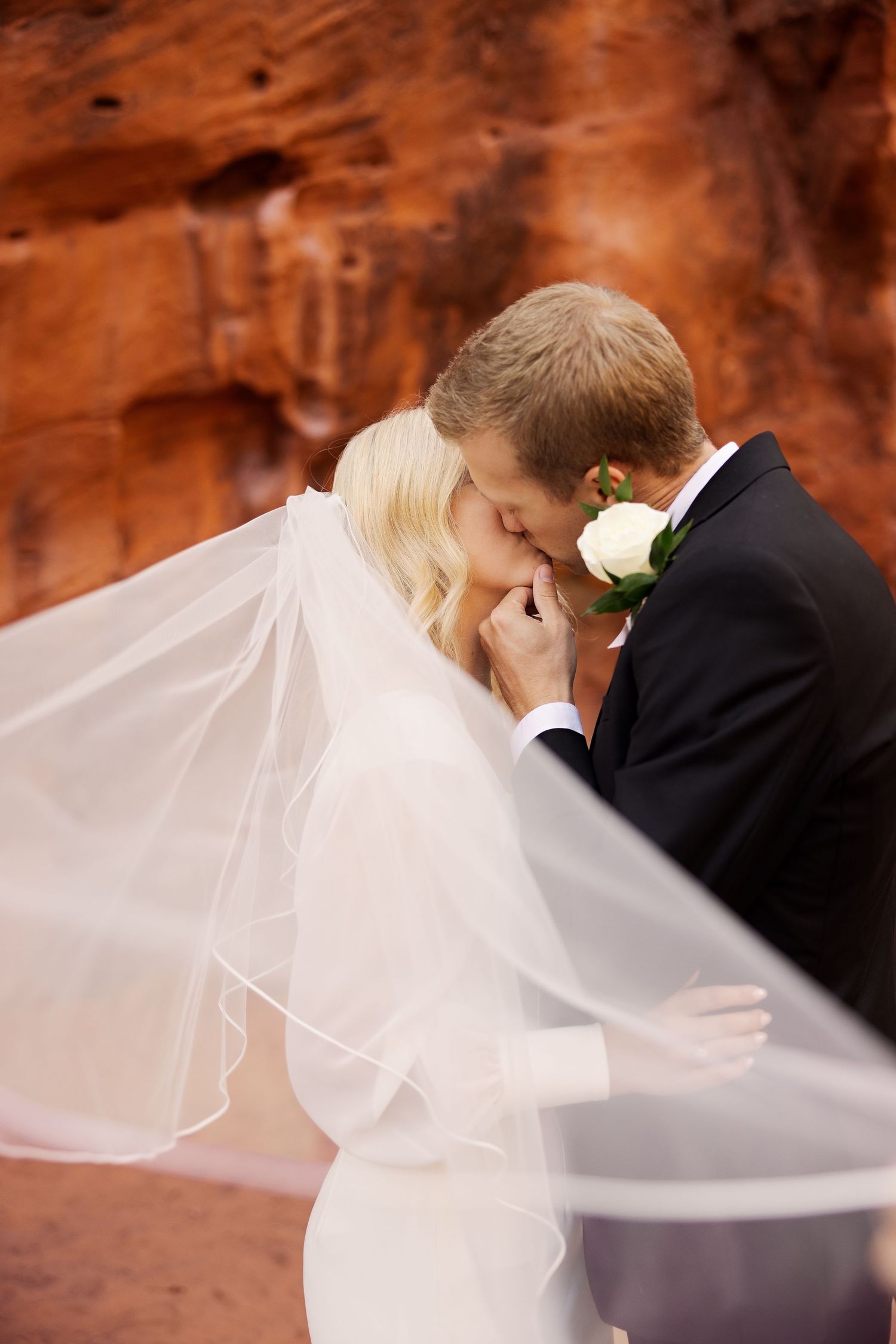 Intimate wedding moment against red rock canyon wall with flowing white veil.