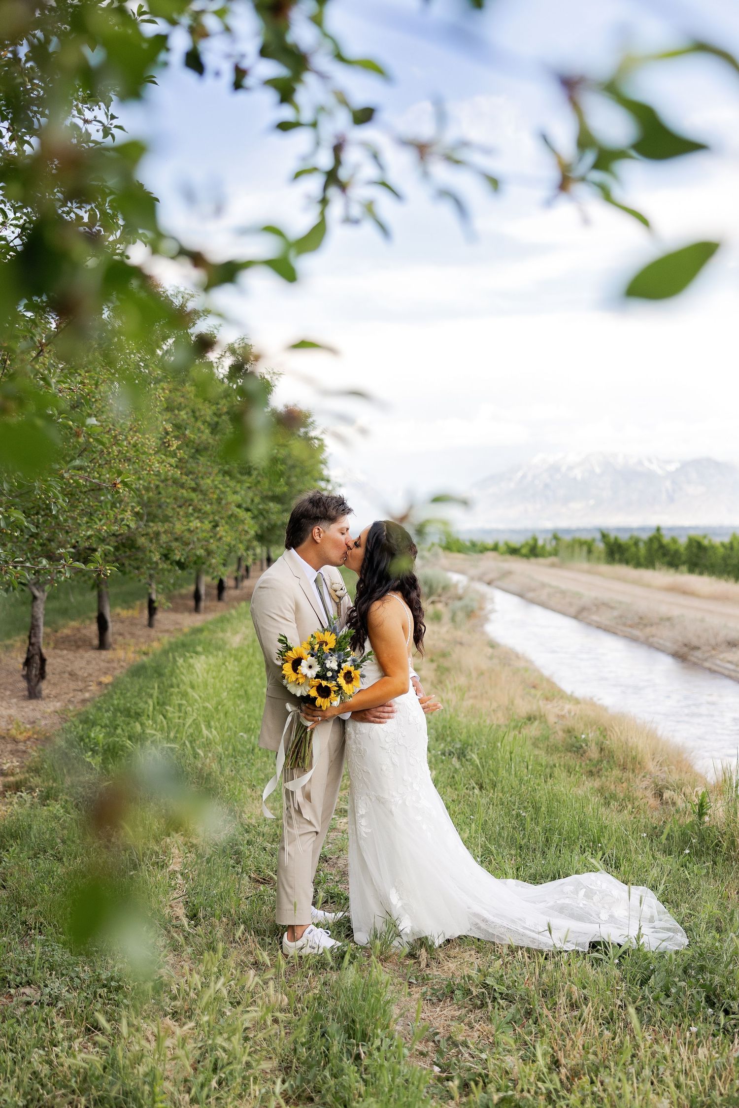 Romantic wedding portrait in orchard with sunflower bouquet and flowing white dress.