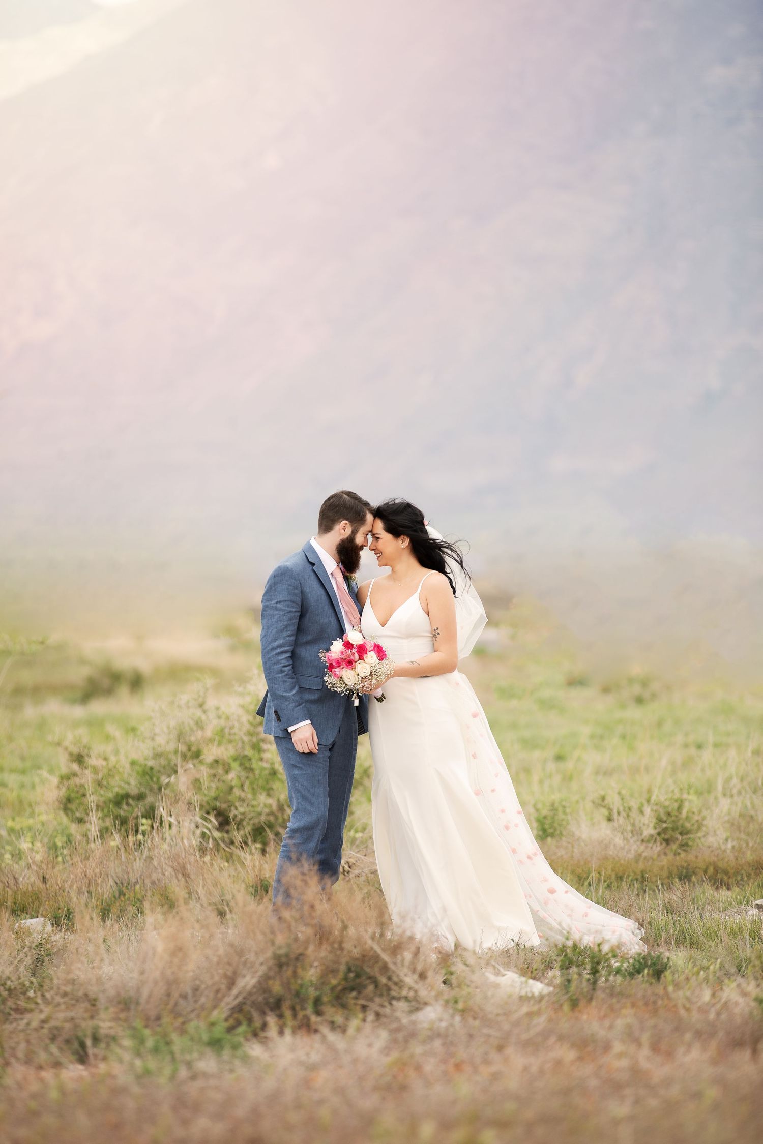 Romantic wedding portrait in misty mountain meadow during golden hour.
