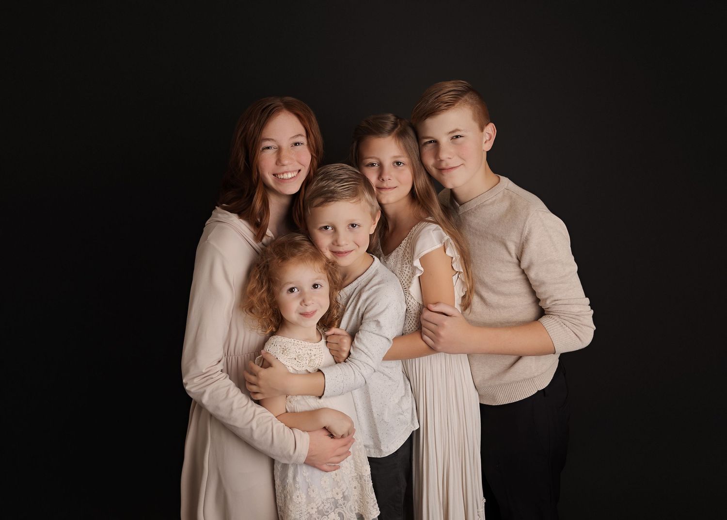 Studio portrait of a family group wearing coordinated neutral tones against a dark background.