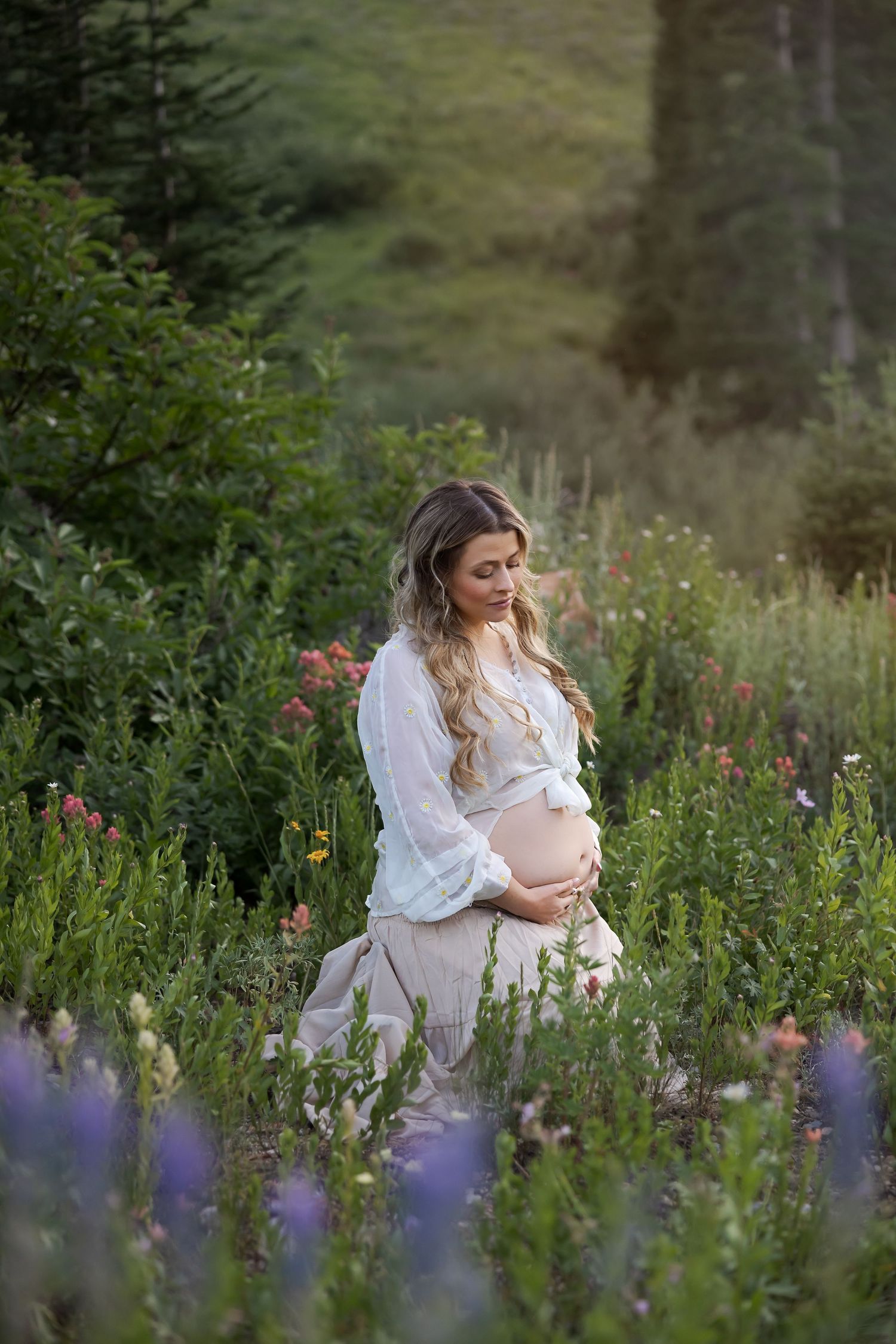 A person in a white dress sits among wildflowers and tall grass in a dreamy outdoor garden setting.